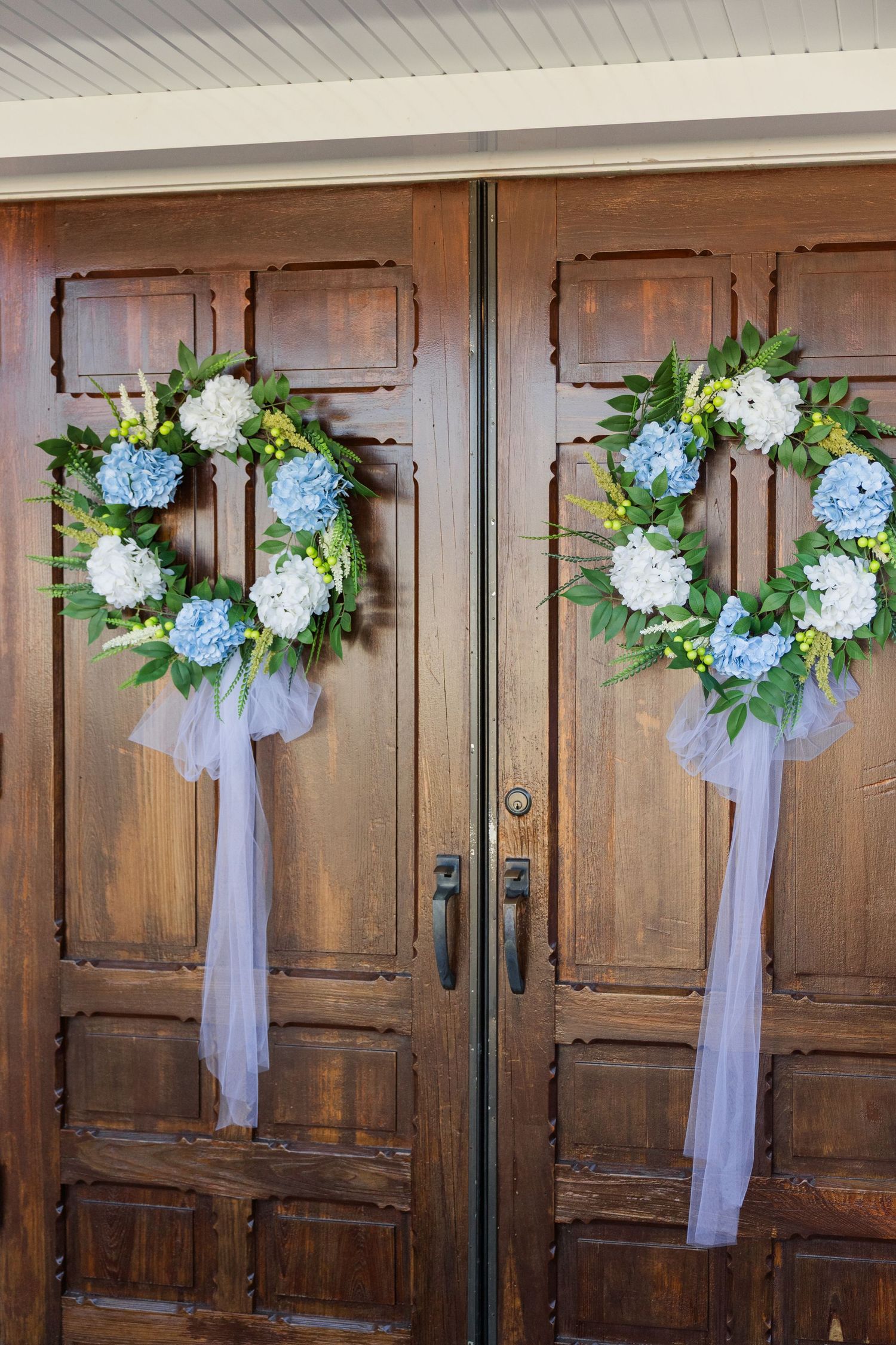 Wooden church doors decorated with matching wreaths of blue and white hydrangeas with flowing tulle ribbons.