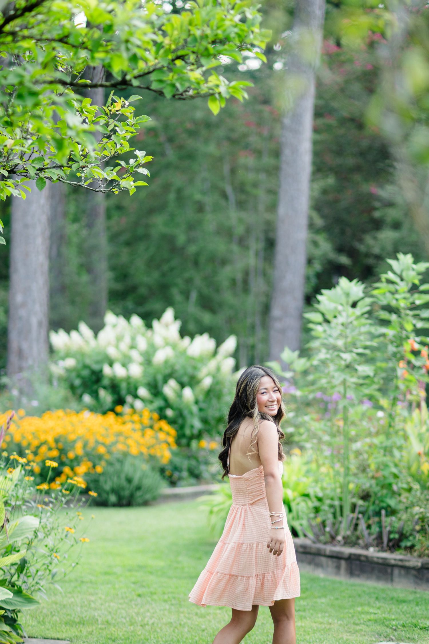 Young woman in peach dress walking through lush green garden with blooming flowers.