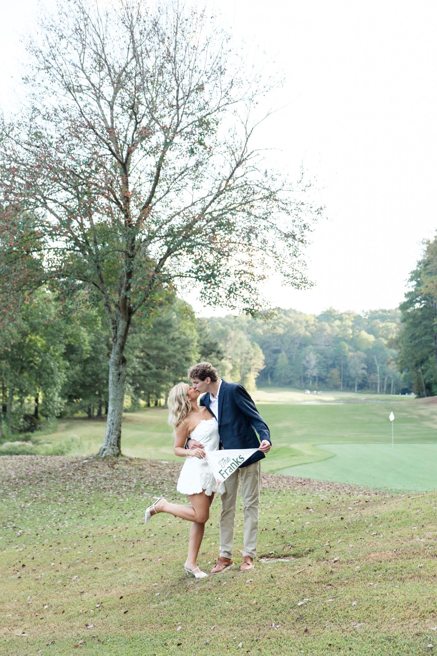 Couple sharing a romantic kiss on a golf course, bride in white dress with groom in navy blazer and khakis.