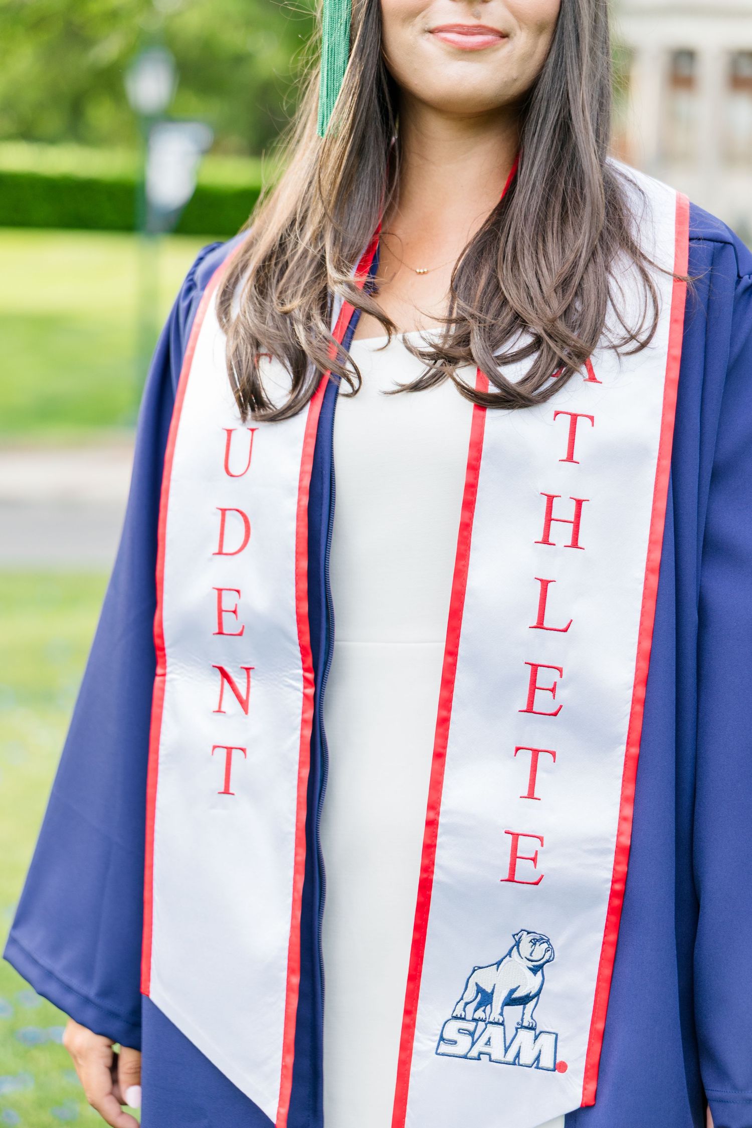Close-up of college graduate wearing blue gown and Student Athlete stole with SAM university bulldog logo.