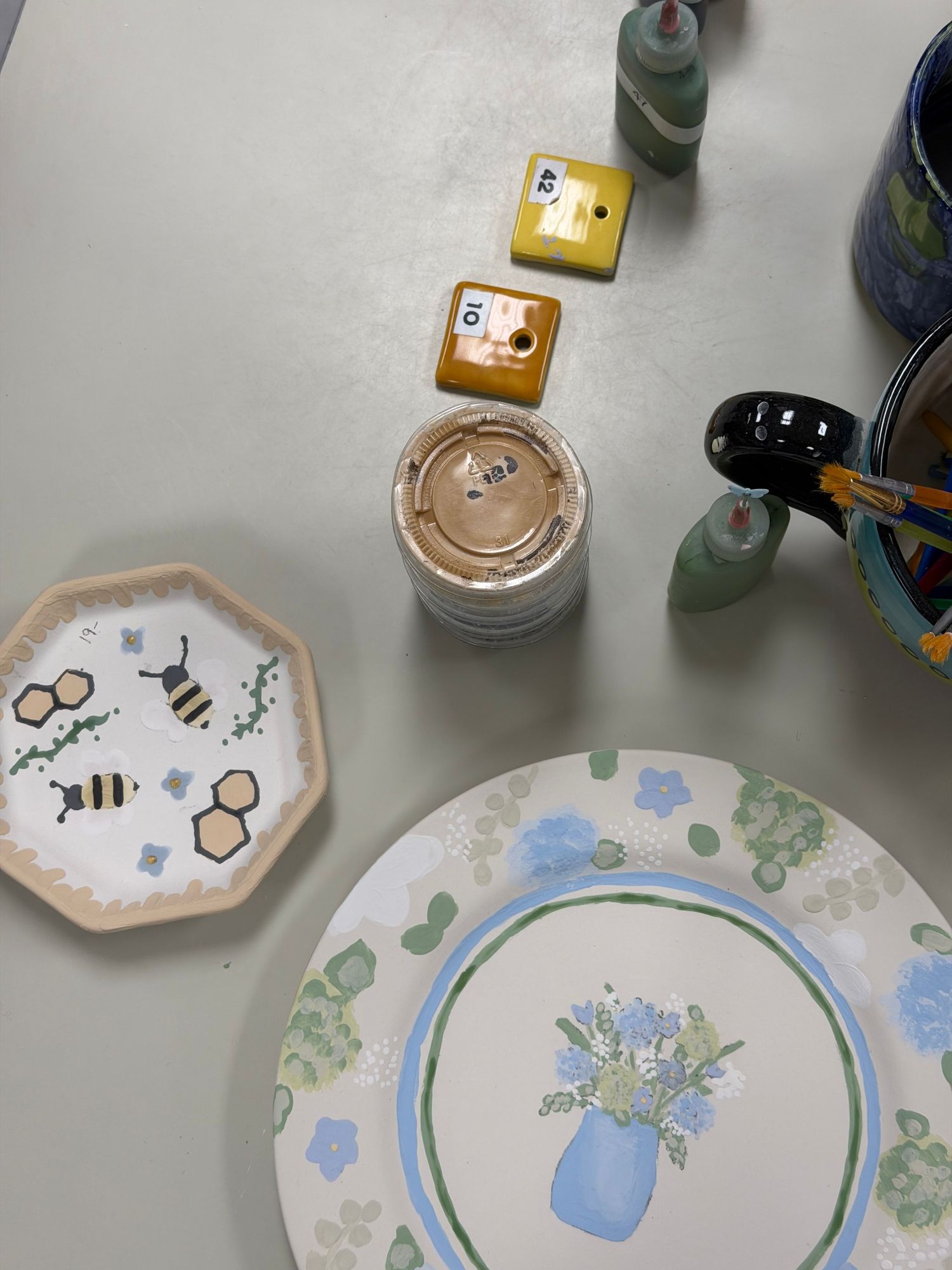 Hand-painted ceramic plates and tiles featuring bees and floral designs on a white table.
