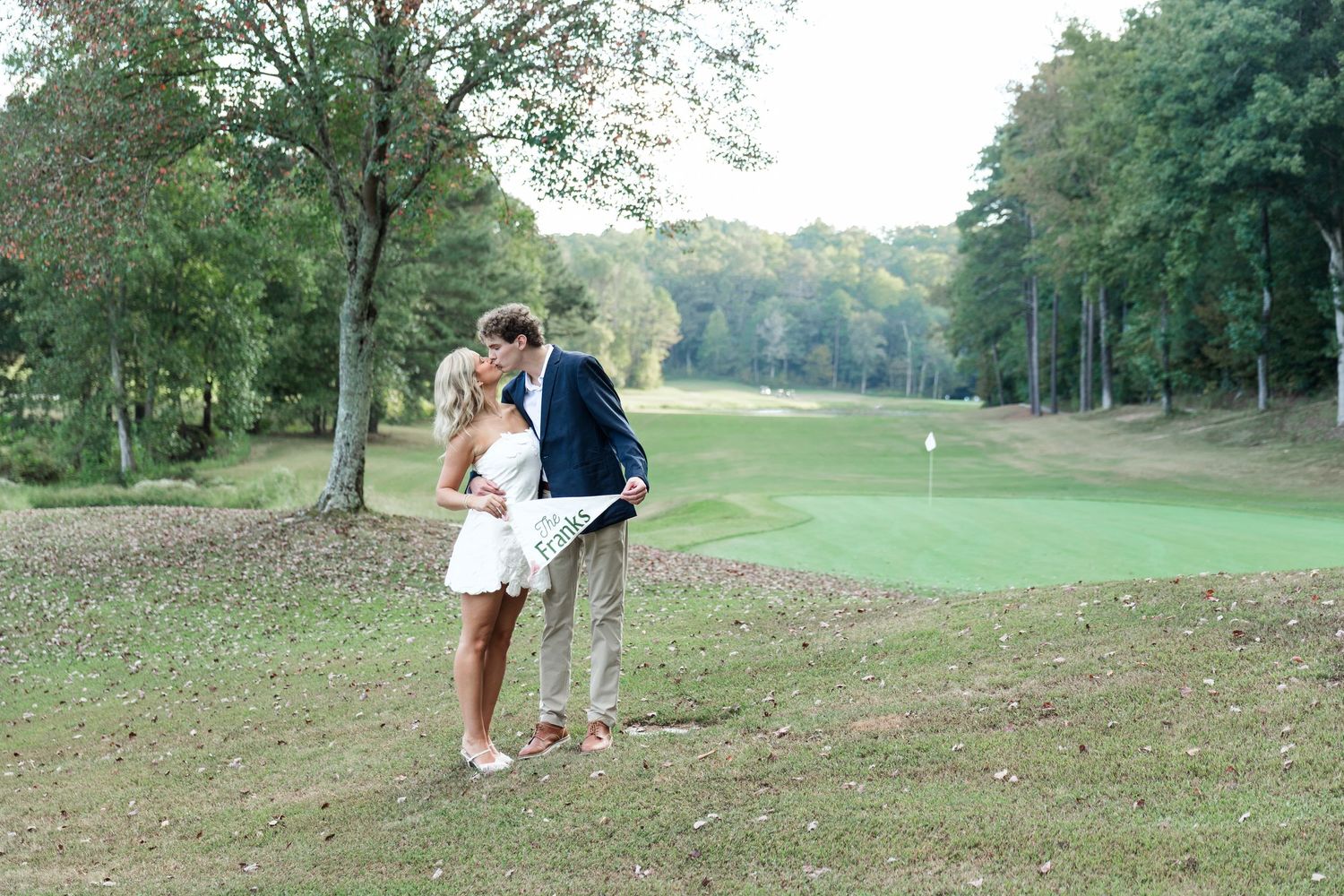 Couple sharing kiss on golf course near sand bunker with green fairway behind.