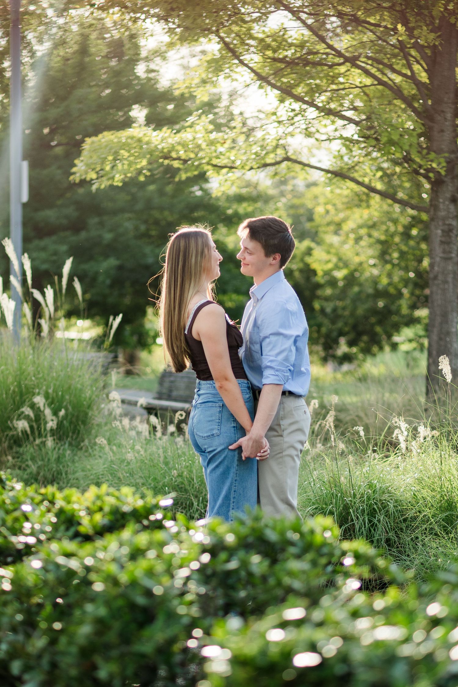 Couple holding hands and smiling at each other in a lush green garden at golden hour.