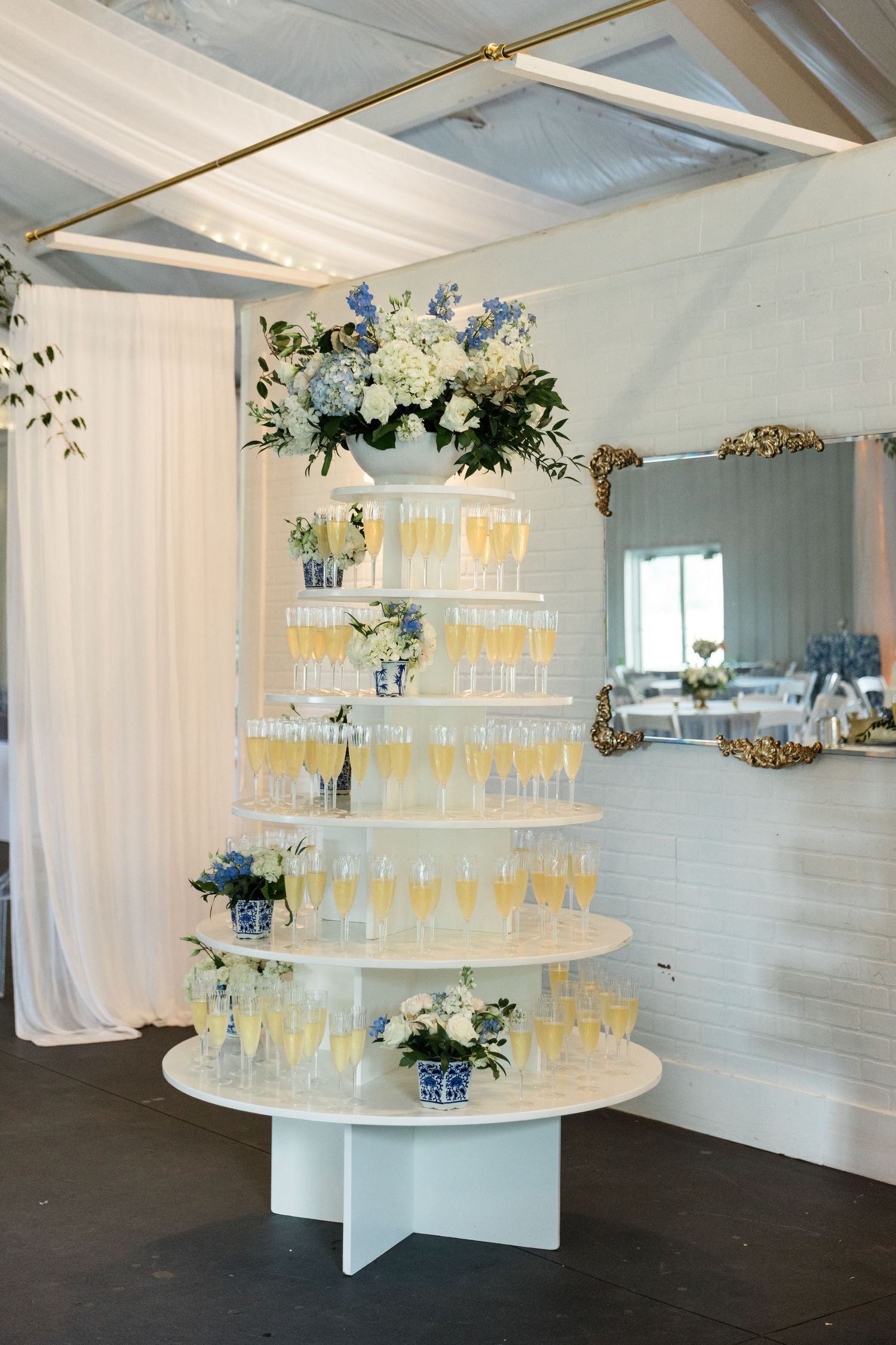 Multi-tiered champagne tower display with blue and white hydrangea floral arrangements at wedding reception.