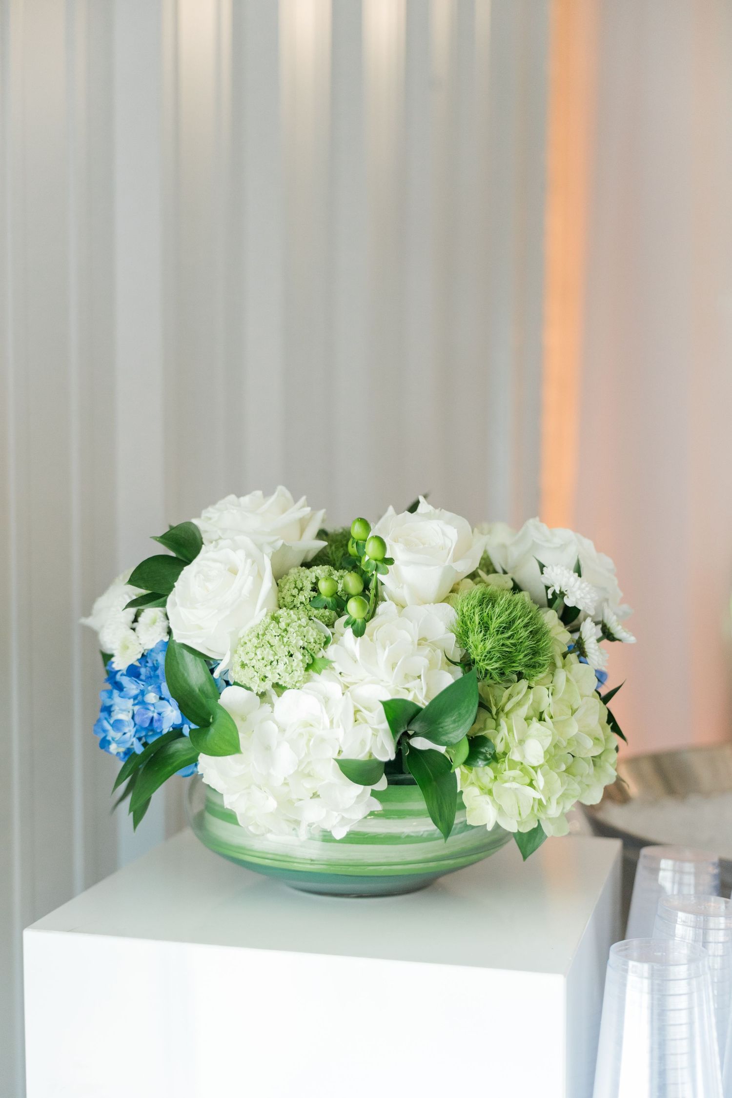 Round striped vase with white roses, hydrangeas, and green accents as wedding floral arrangement.