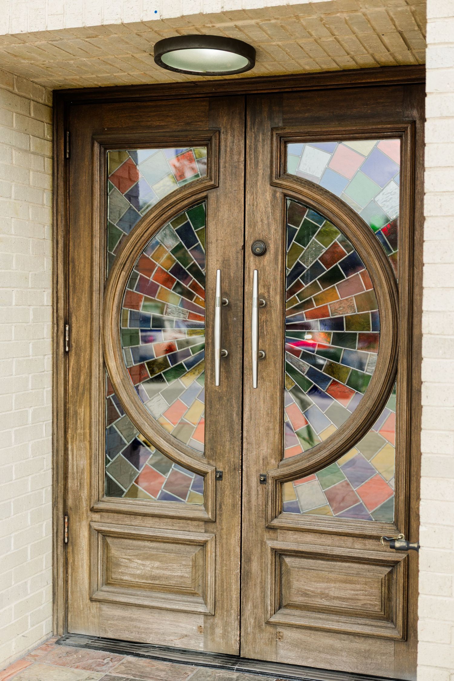 Elegant wooden double doors with colorful stained glass mosaic panels and circular window design.