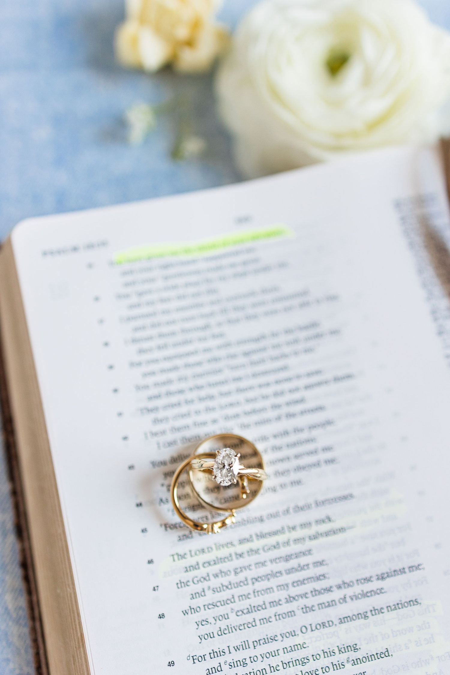 Gold diamond engagement ring and wedding band resting on open Bible page with highlighted scripture verse.