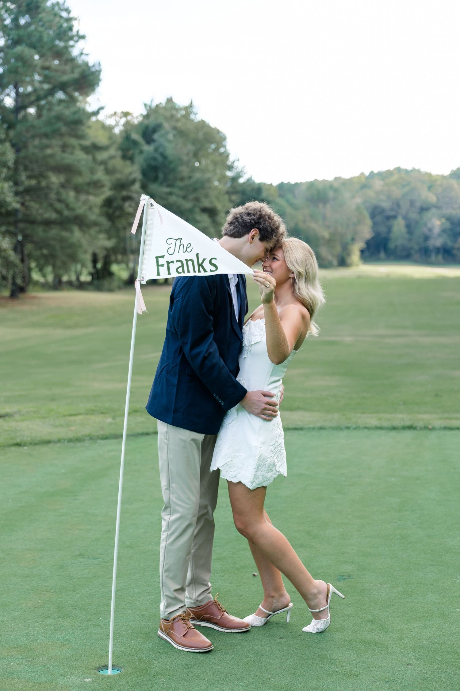 Couple sharing a kiss beside a custom The Franks golf flag on a green golf course fairway.