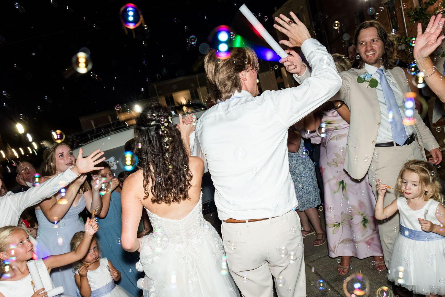 Bride and groom celebrating with bubbles and guests during lively outdoor wedding reception.