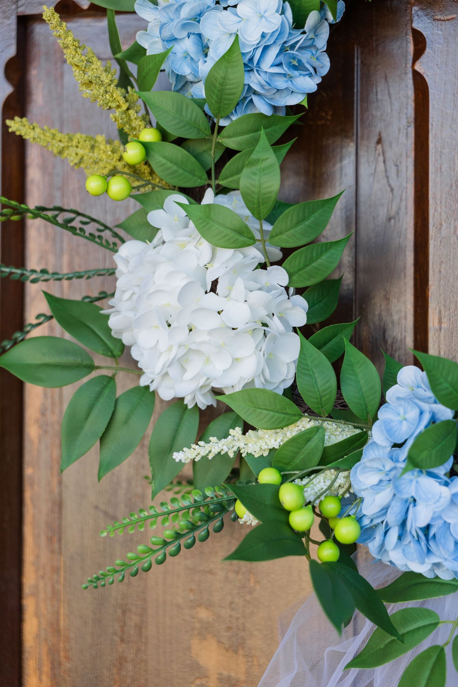 Blue and white hydrangea wedding floral arrangement with green berries on wooden backdrop.