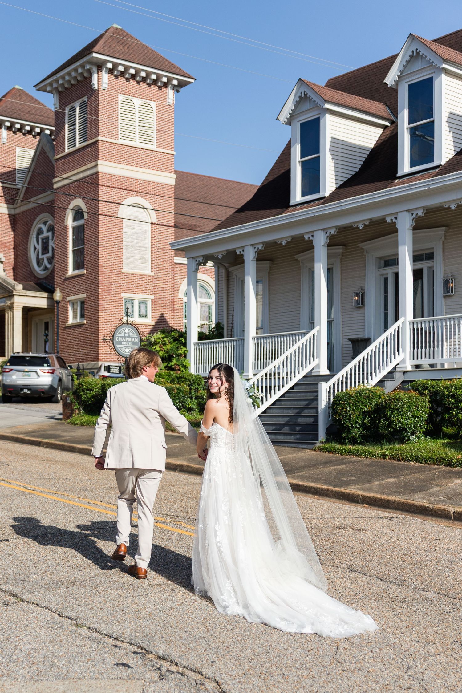 Bride and groom walking hand-in-hand on a street near a historic brick church.