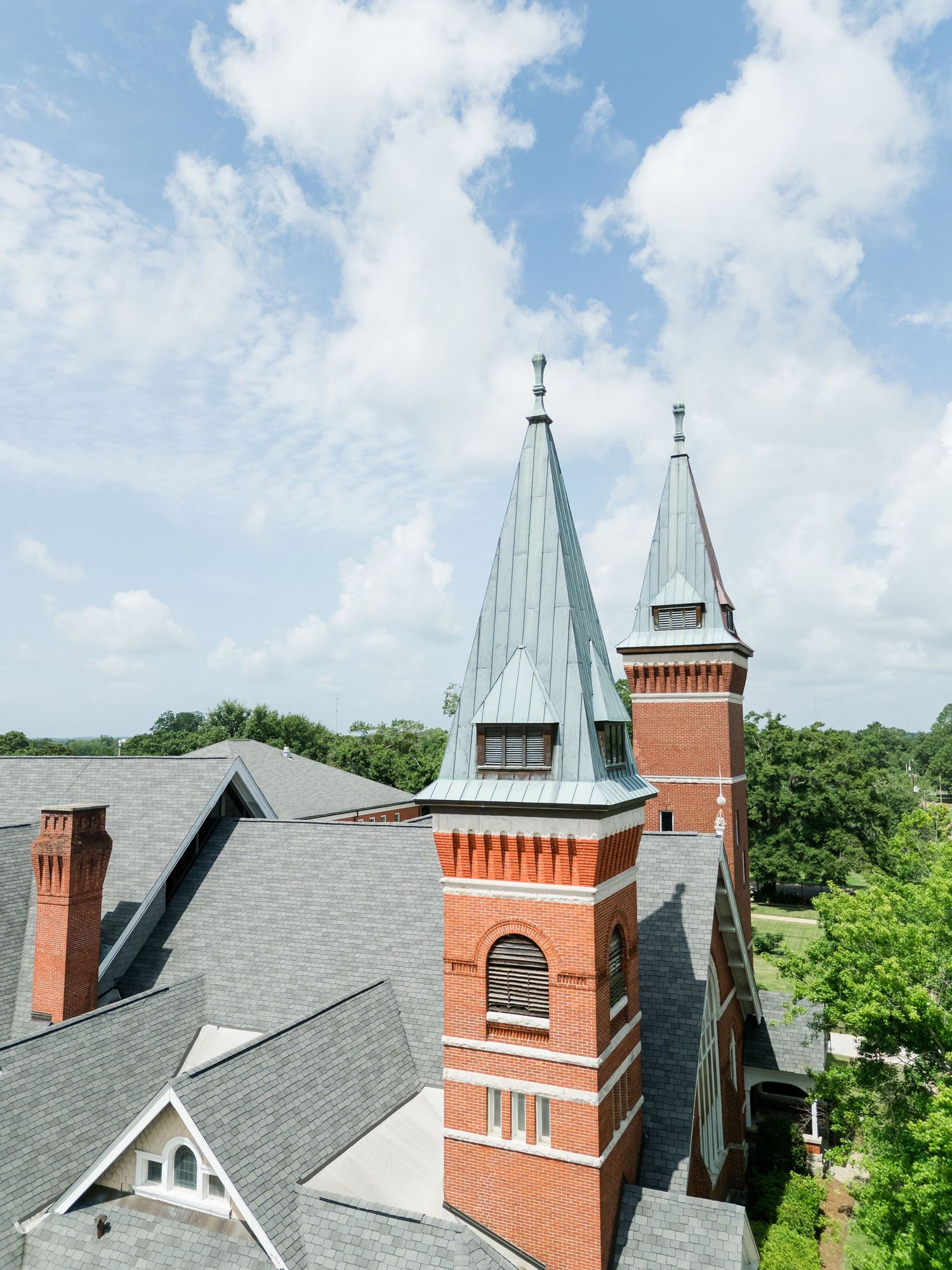 Aerial view of historic red brick church with green copper spires against a blue sky with white clouds.