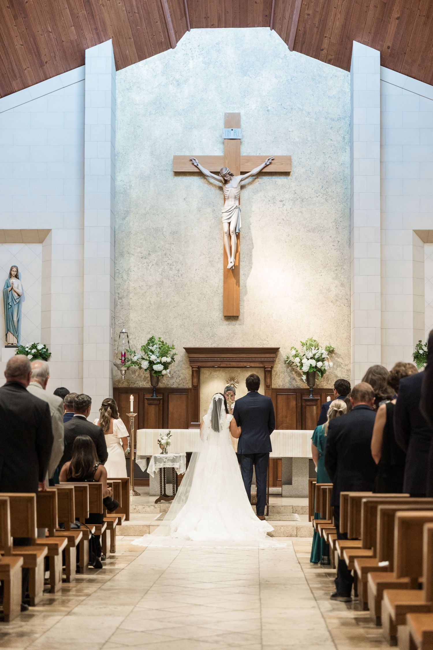 Bride and groom standing at altar beneath crucifix during Catholic wedding ceremony.