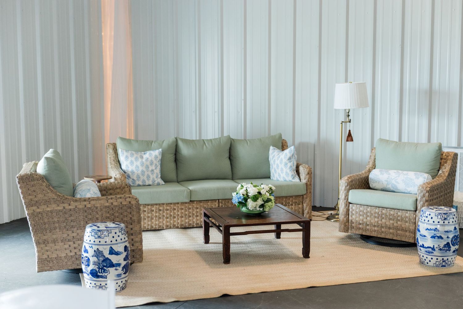 Wicker lounge furniture with sage green cushions and blue and white garden stools at wedding venue.
