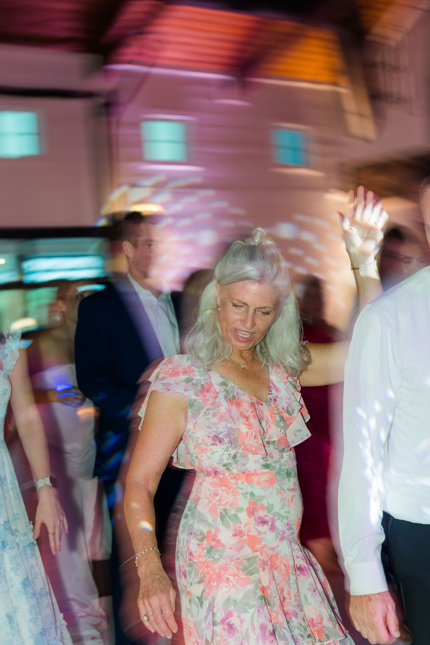 Wedding guests dancing with motion blur under colorful reception lighting.