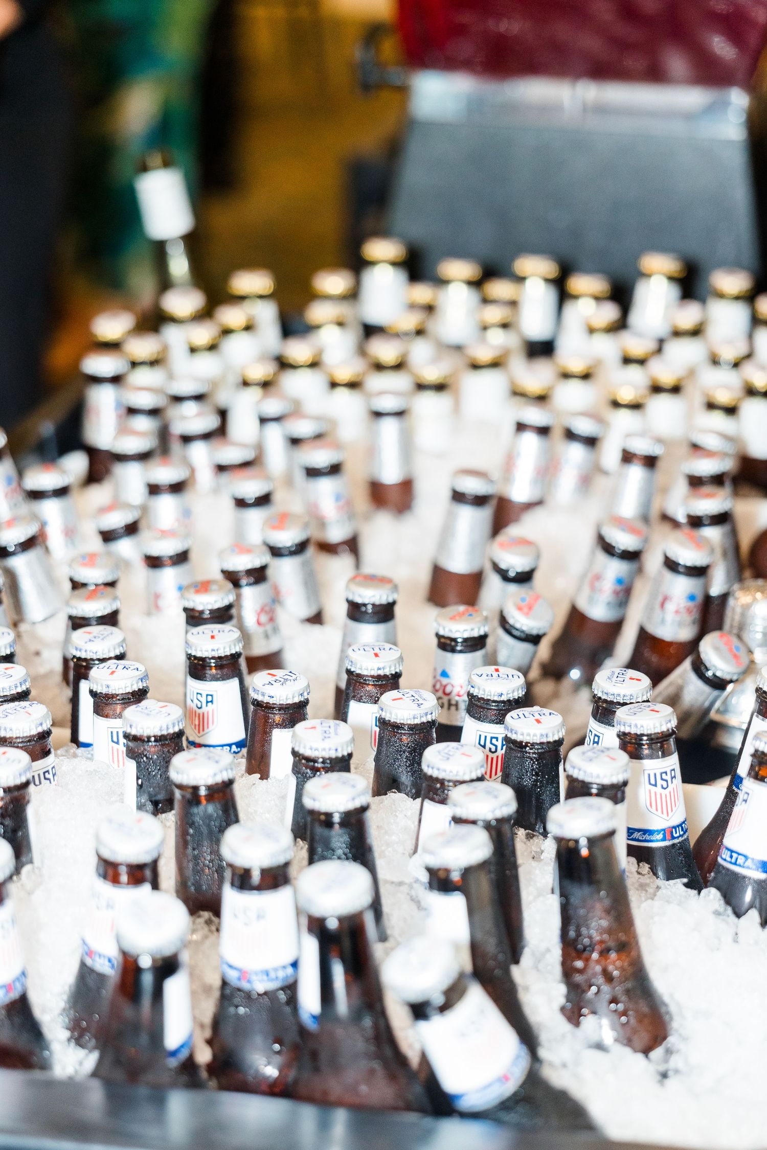Rows of chilled beer bottles packed in ice at an outdoor wedding reception bar.