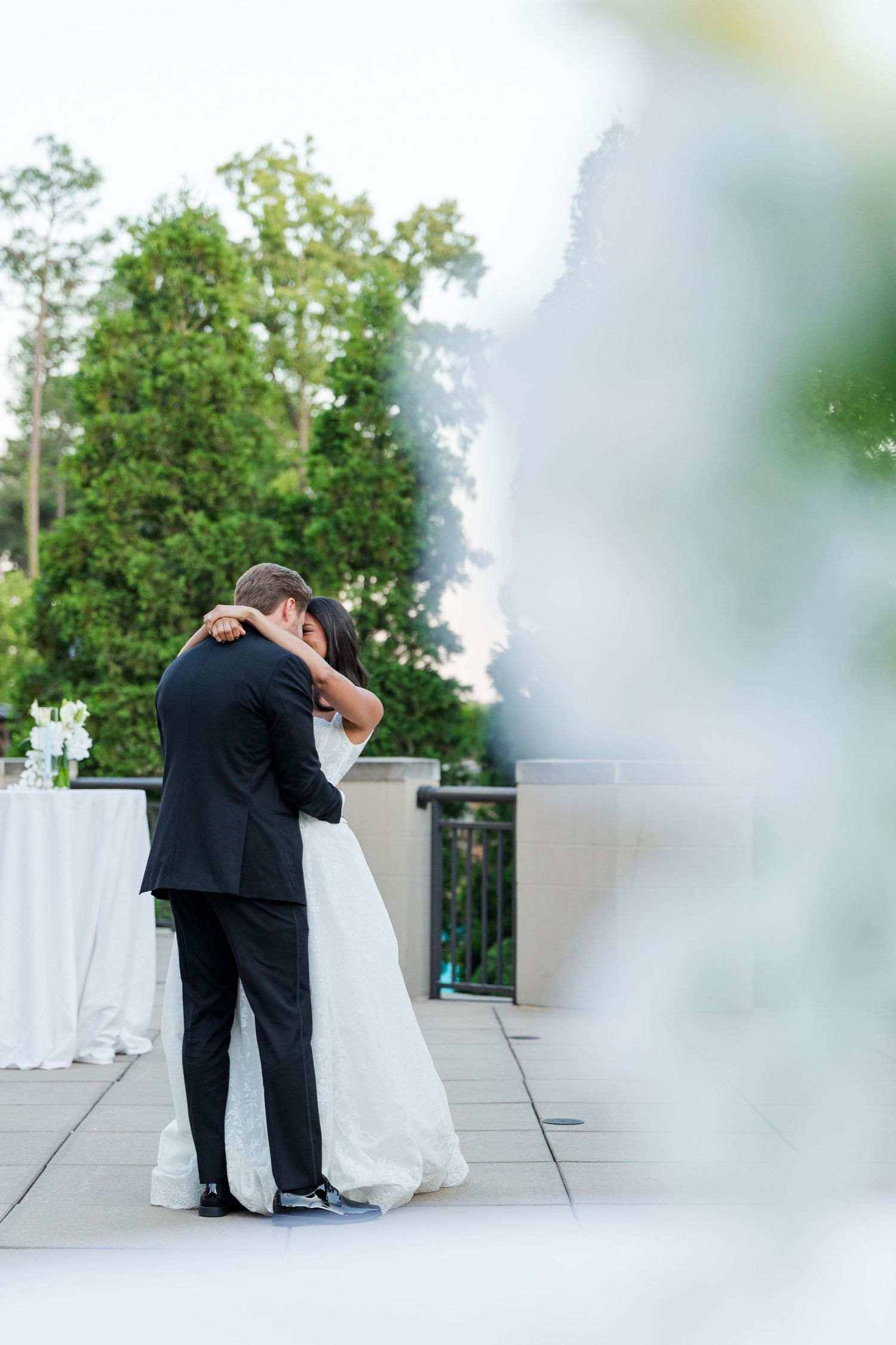 Bride and groom share first dance on outdoor terrace, surrounded by lush greenery at elegant wedding reception.