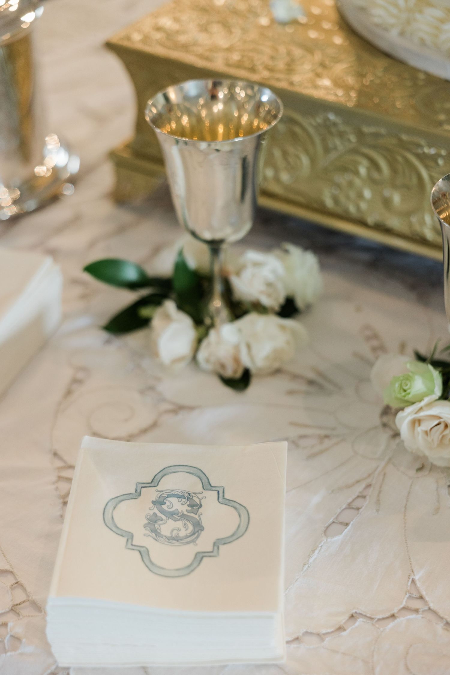Elegant wedding reception table detail featuring a monogrammed napkin, silver goblet, and white roses.