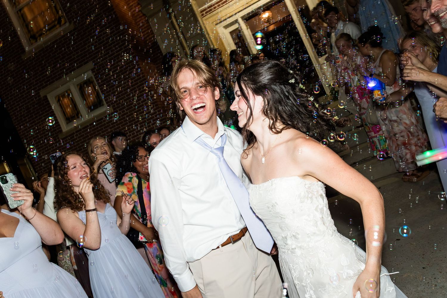 Newlyweds dance joyfully surrounded by bubbles and cheering guests during their lively wedding reception celebration.