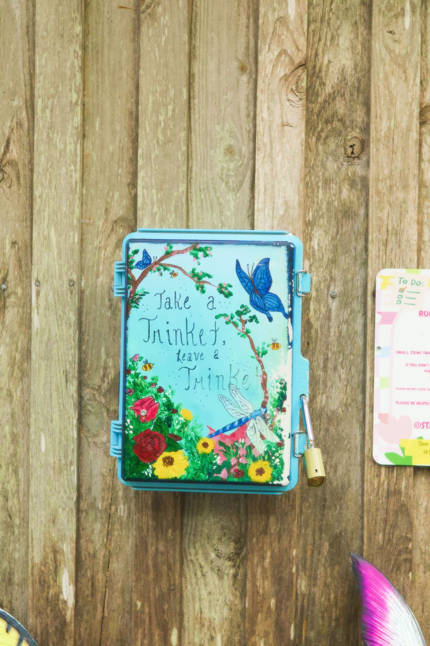 Decorative blue trinket box painted with butterflies and flowers mounted on wooden fence.