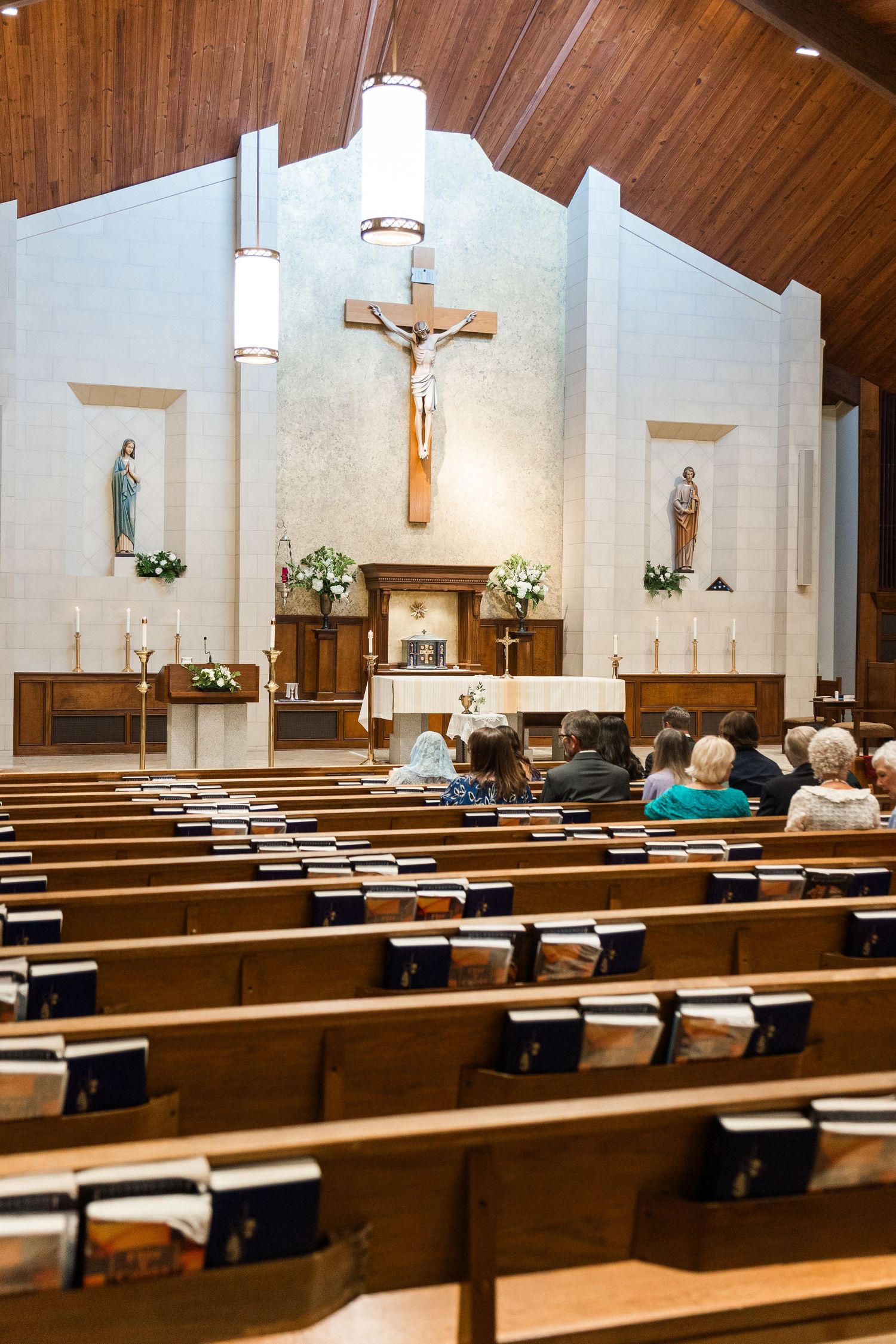 Catholic church interior with wooden pews, crucifix altar, and congregation gathered for Mass.