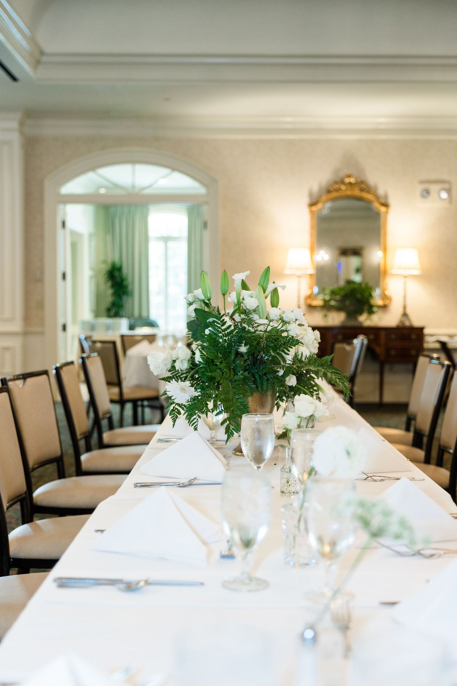 Elegant wedding reception table set with white linens, floral centerpieces, and glassware in a classic ballroom.