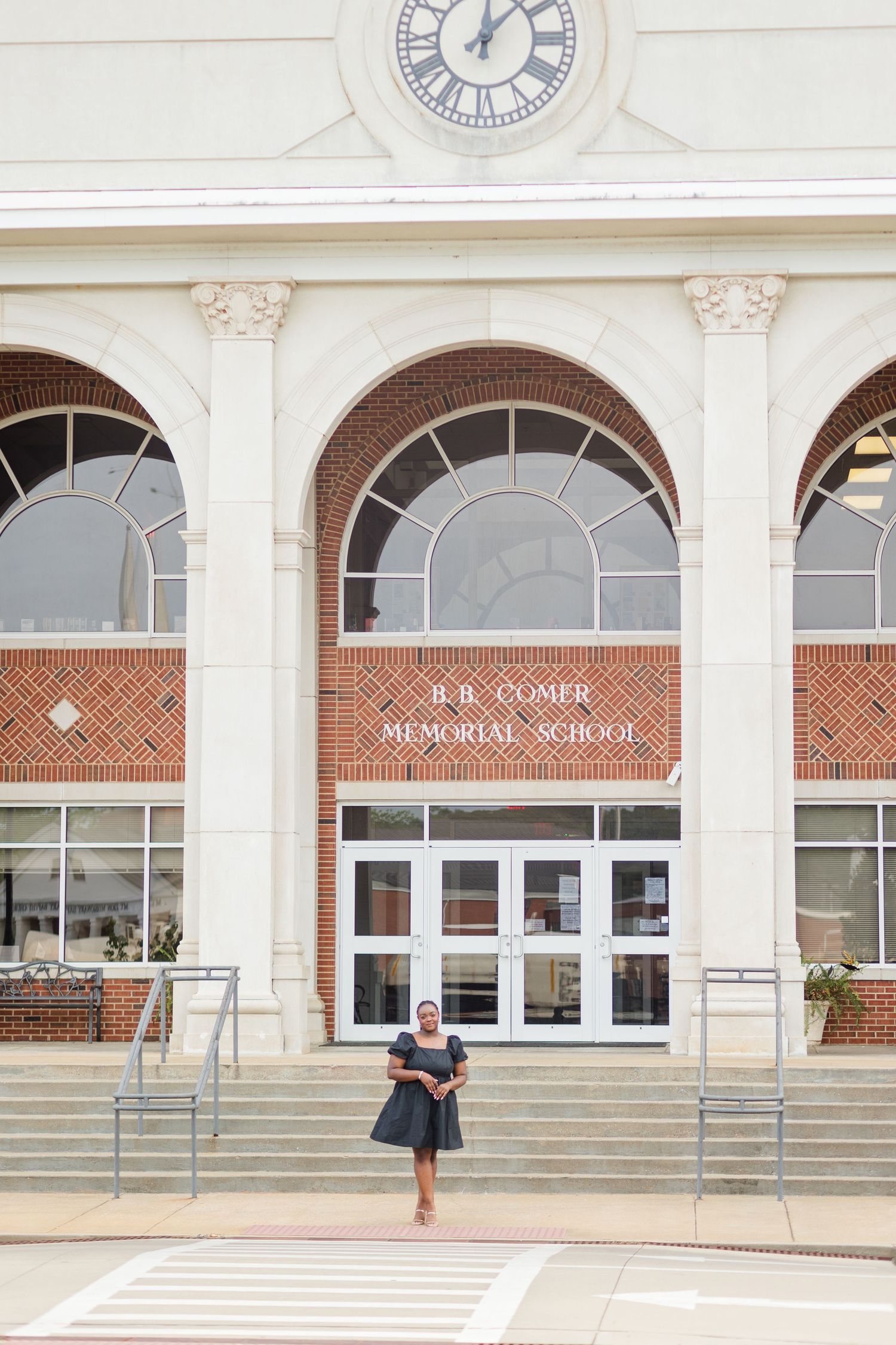 A woman stands on steps in front of B.B. Comer Memorial School, a brick building with arched windows and a clock tower.