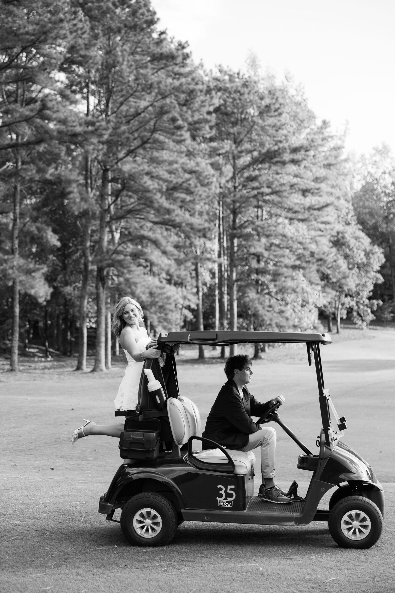 Black and white photo of couple riding golf cart number 35 through wooded course.
