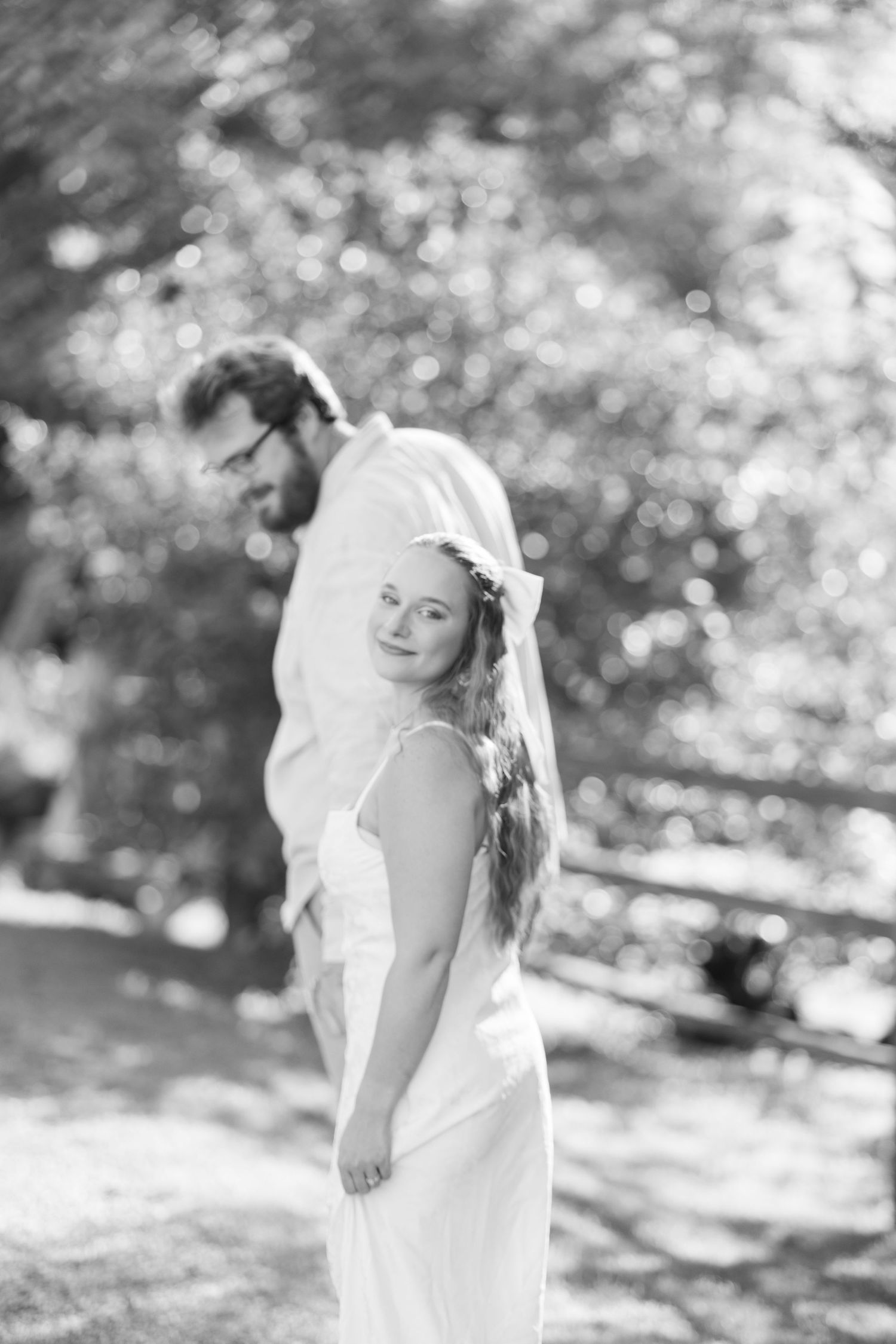 Black and white wedding photo of smiling bride in white dress and veil with groom outdoors.
