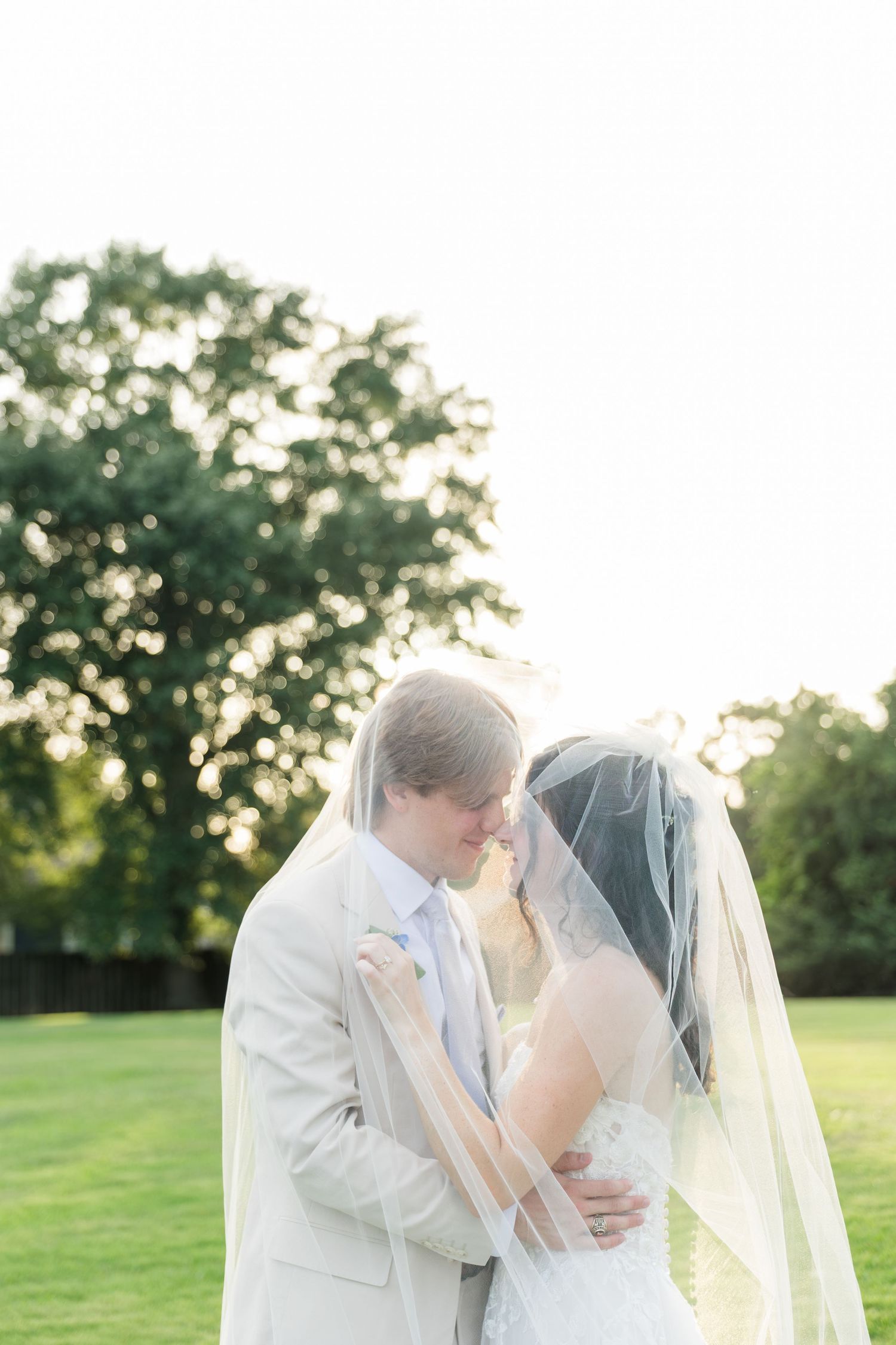 Bride and groom sharing an intimate moment under a flowing veil at golden hour.