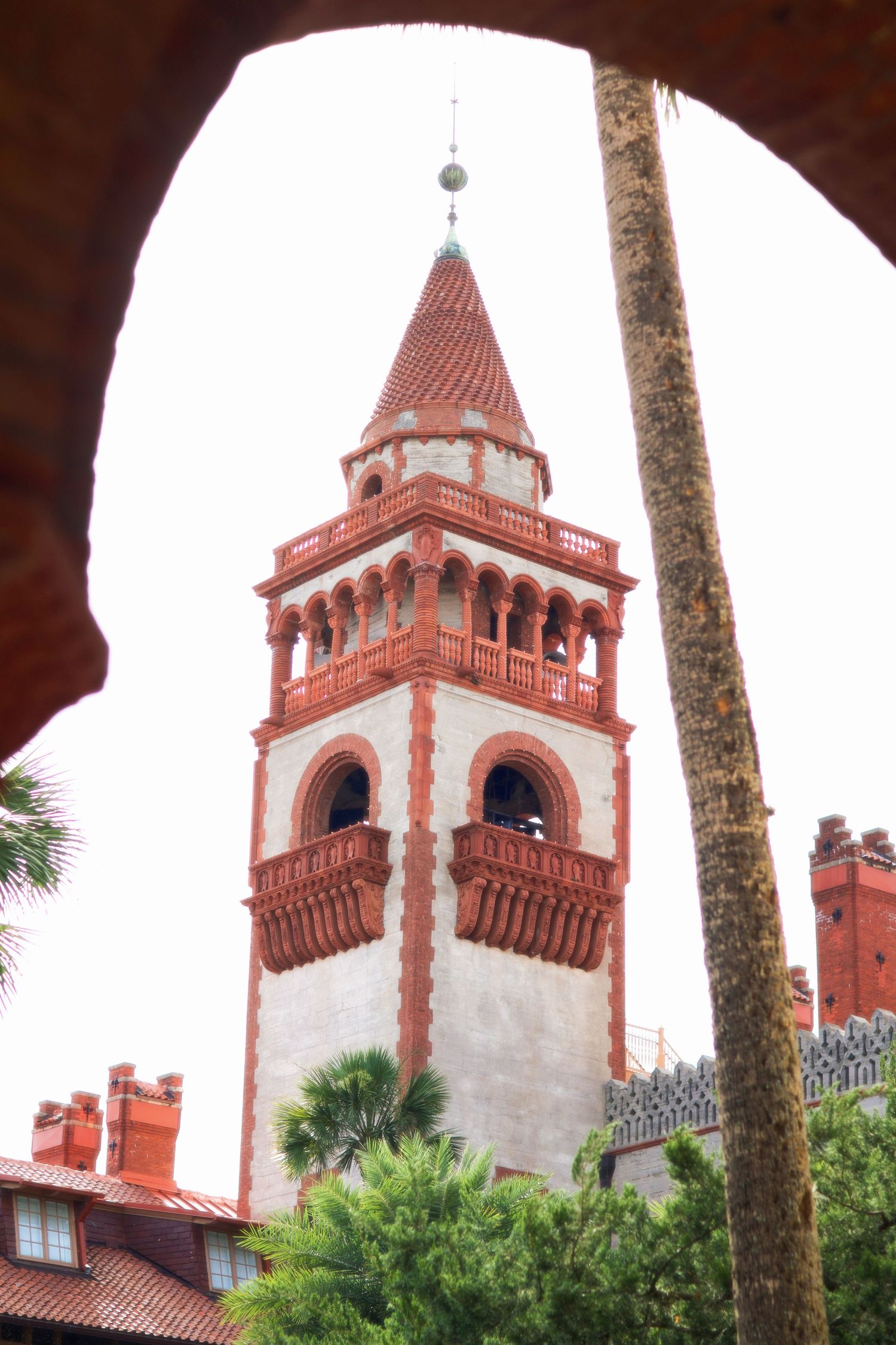 Ornate red and white tower of Flagler College rises above lush green trees in St. Augustine.