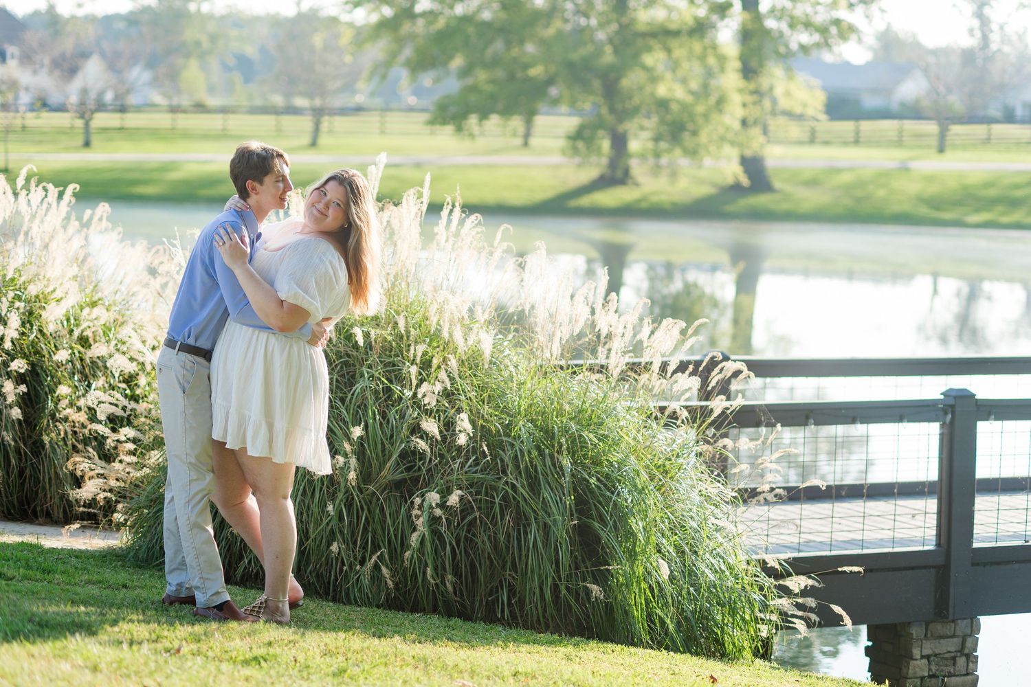Couple embracing romantically near a pond and tall ornamental grasses on a sunny day at a golf course.