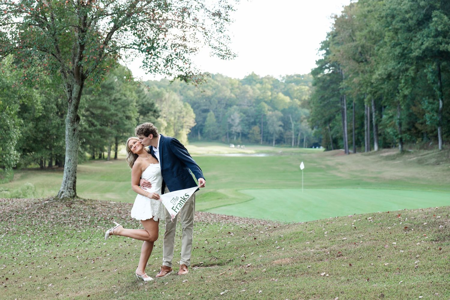 Couple sharing romantic dip kiss near golf course bunker with green in background.