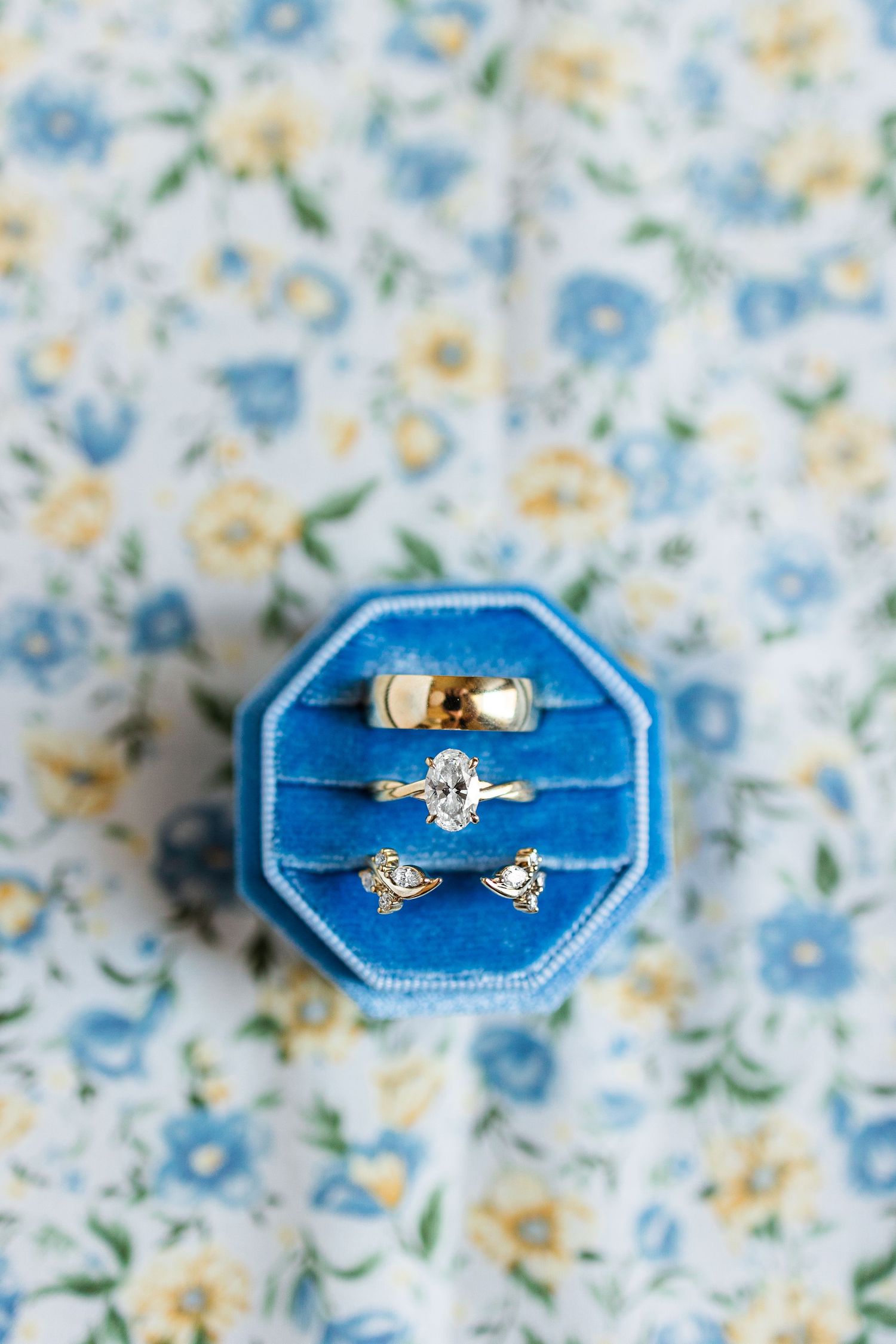 Three gold rings displayed in a blue velvet octagonal ring box on a floral background.