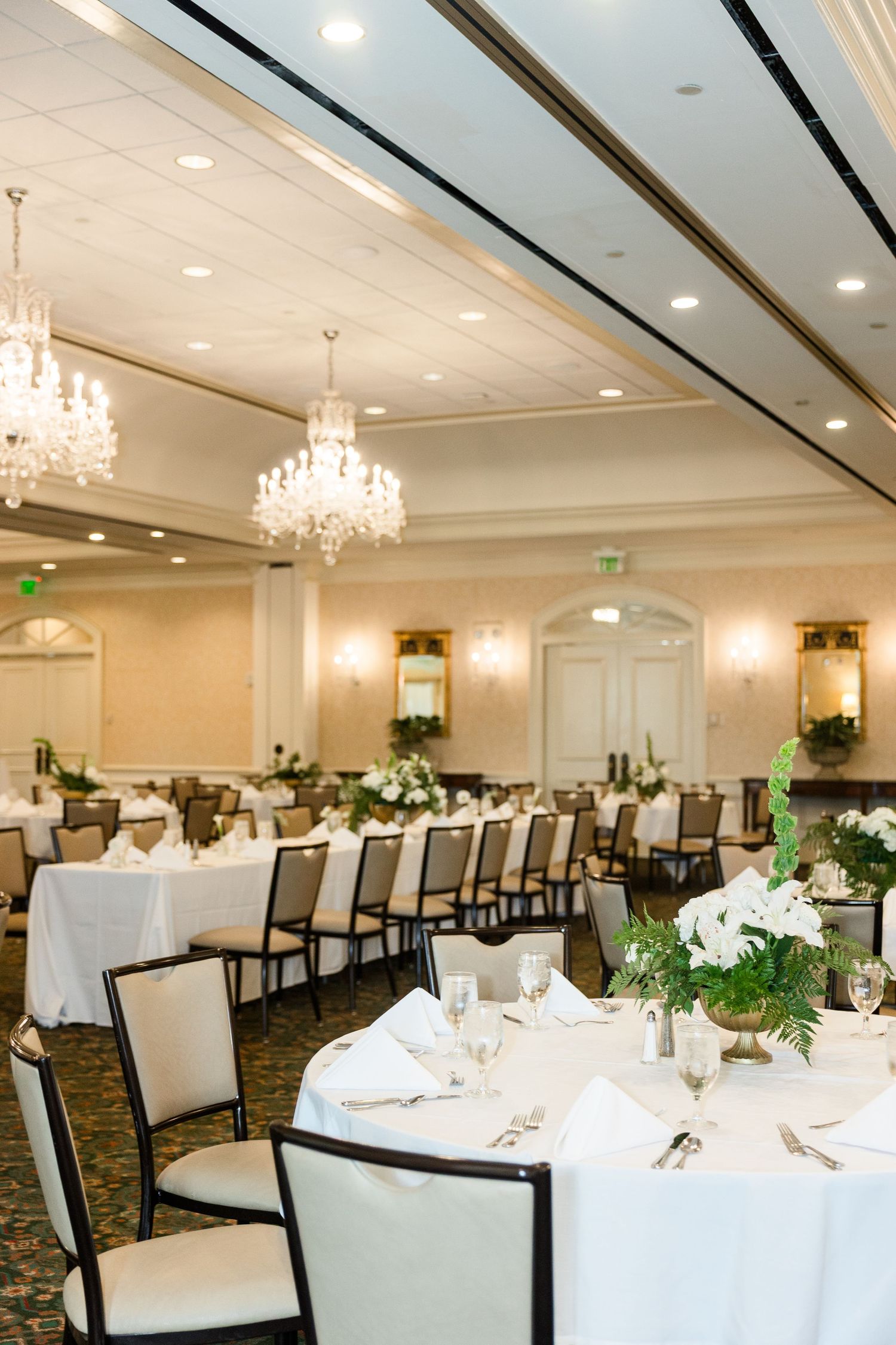 Elegant wedding reception ballroom with crystal chandeliers, white tablecloths, and green floral centerpieces.