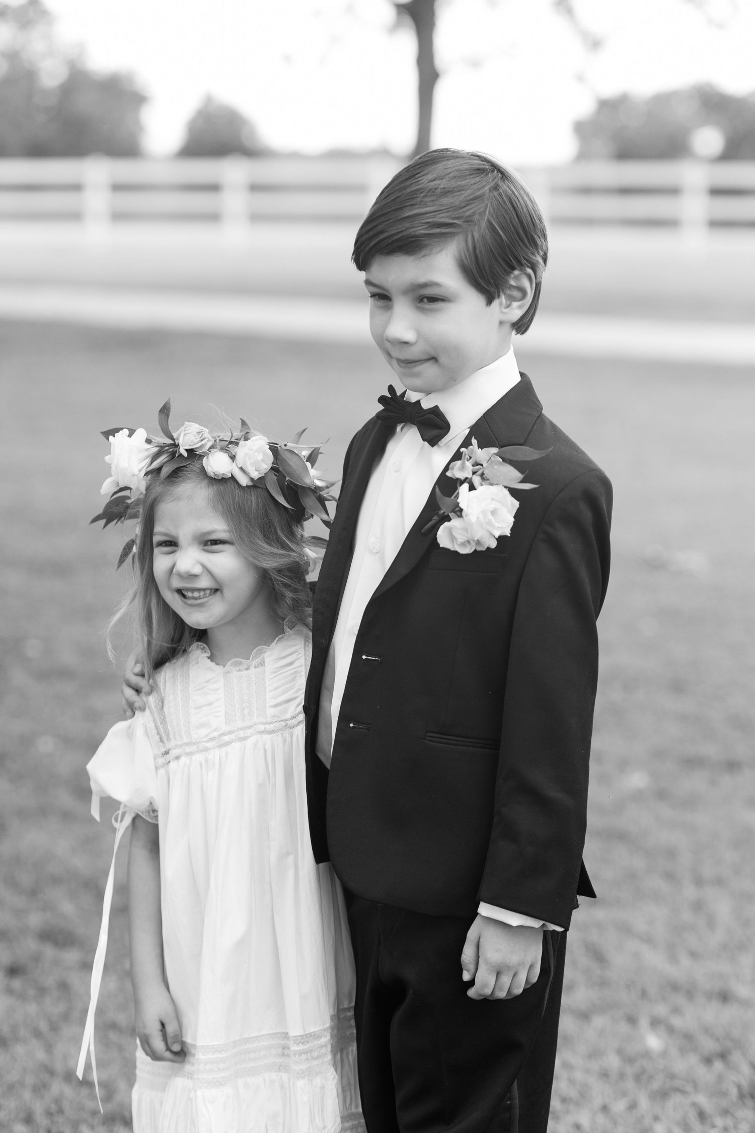 Black and white photo of flower girl with floral crown and ring bearer in tuxedo at wedding.