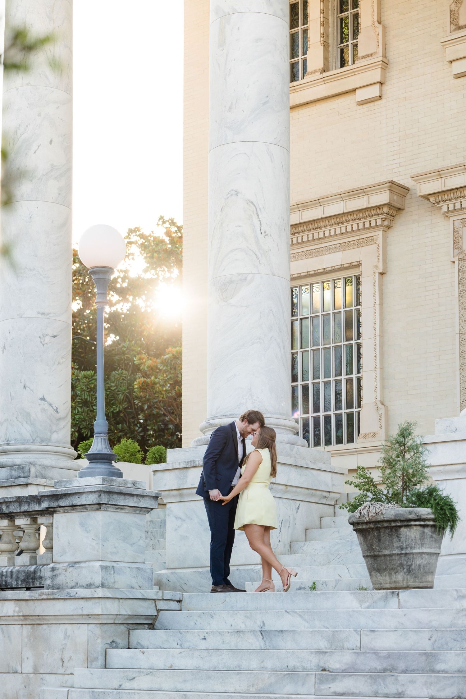 Couple sharing a romantic kiss on marble steps of an elegant building at golden hour sunset.