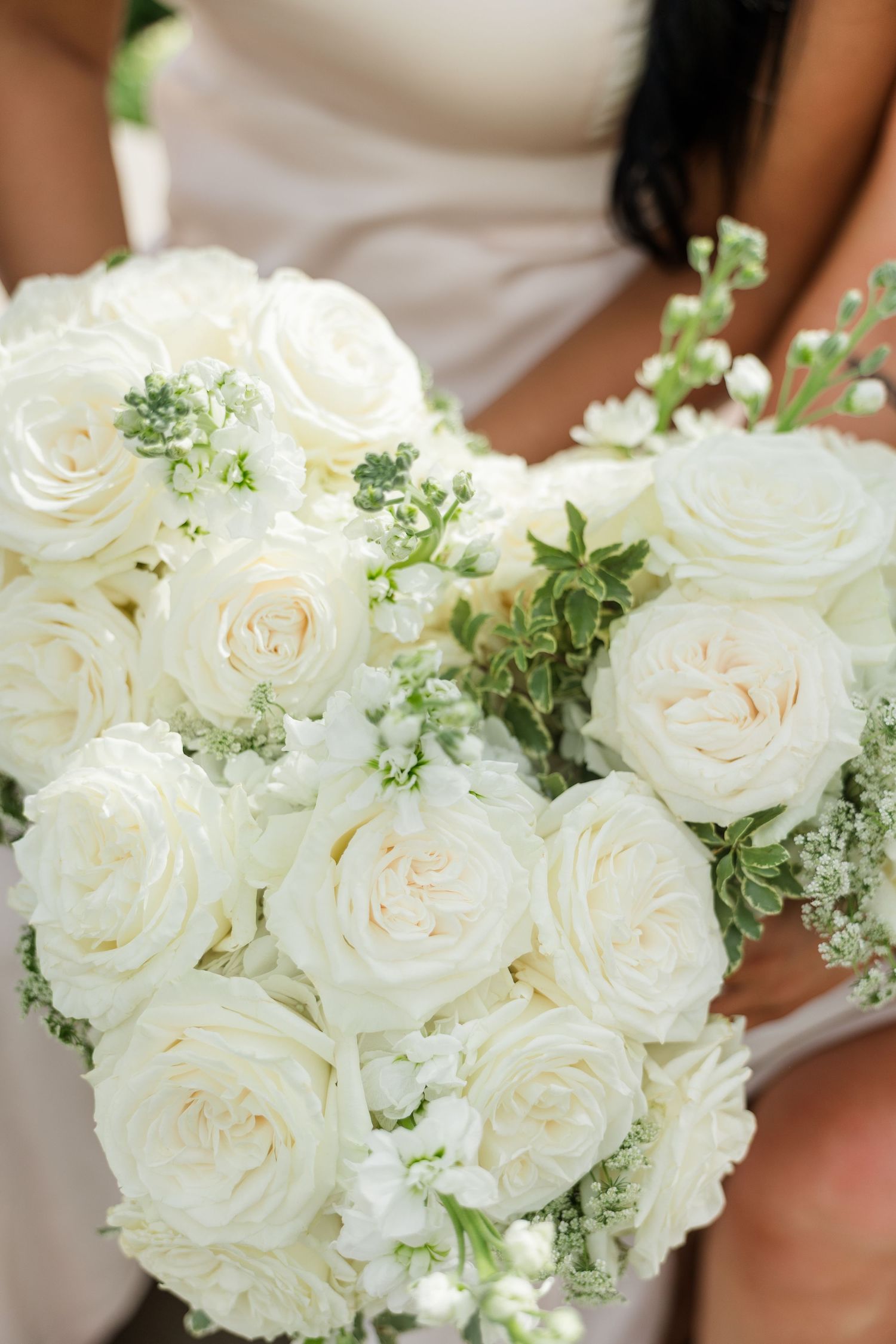 Bride holding a lush bridal bouquet of white roses and greenery accents at a wedding ceremony.