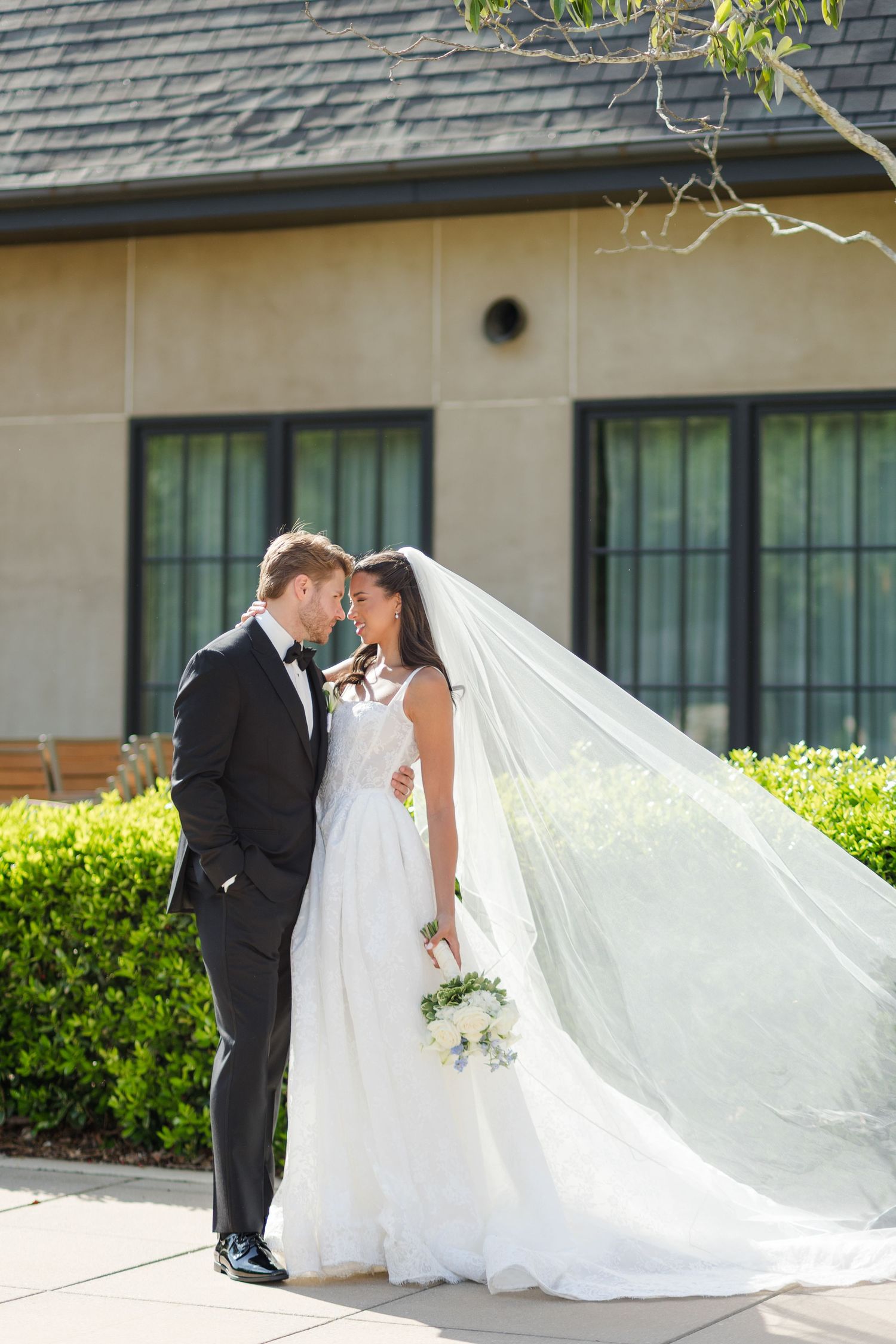 Bride and groom sharing an intimate moment outdoors, with flowing veil blowing in the breeze.