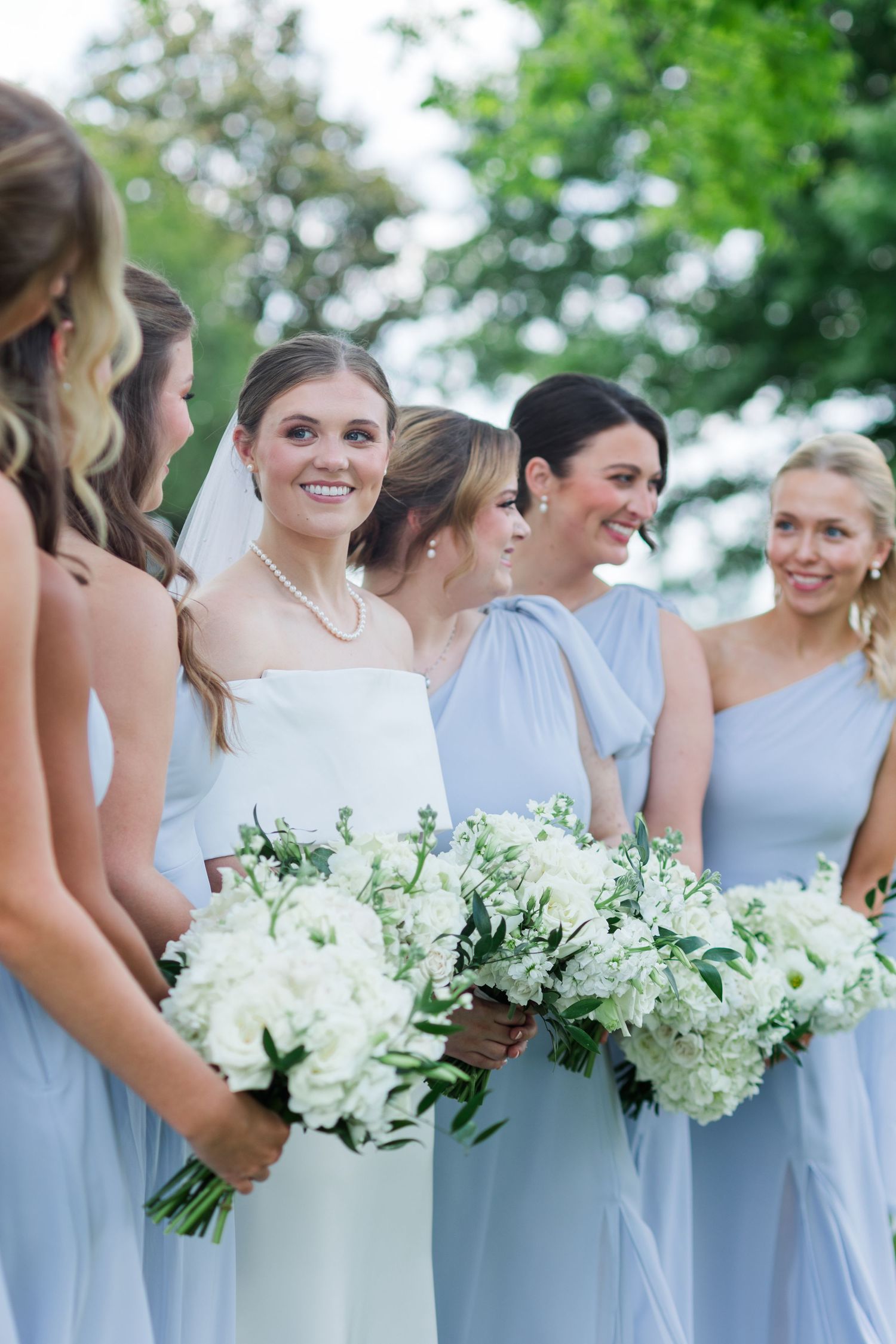 Bride in white strapless gown with bridesmaids in light blue dresses holding white bouquets.