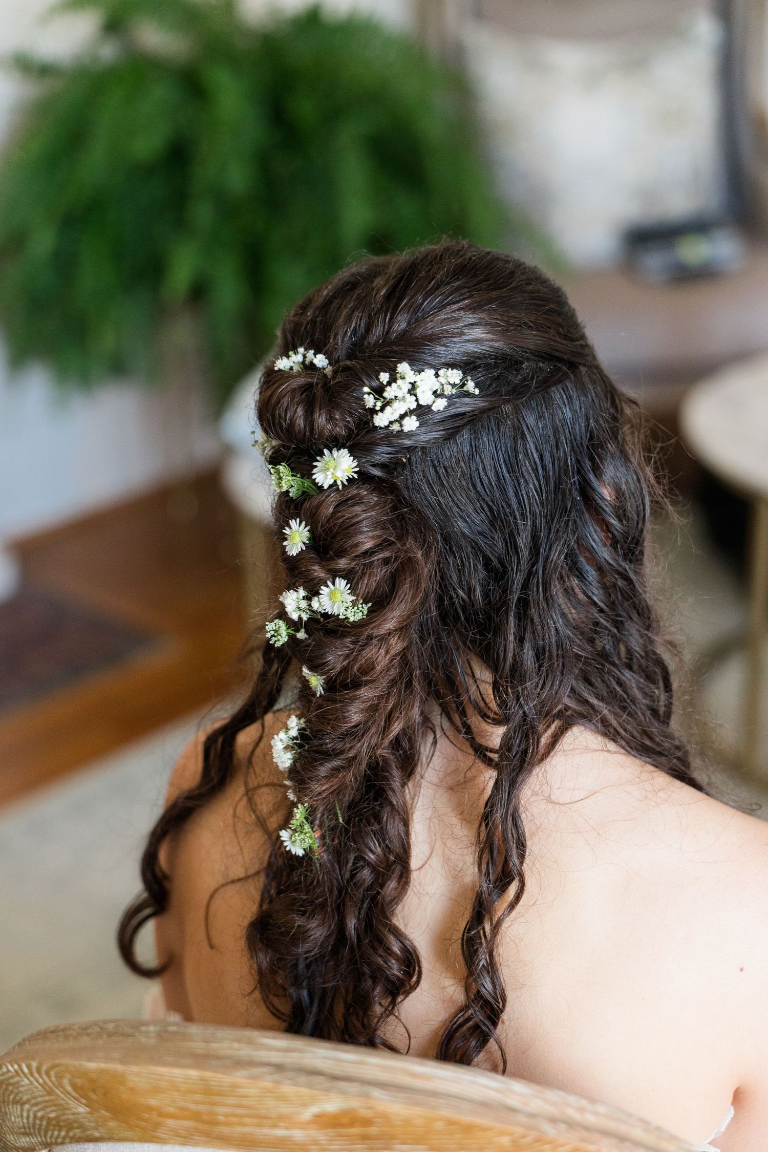 Bride with dark hair styled in a half-up braided hairstyle adorned with small white daisy flowers and baby's breath.
