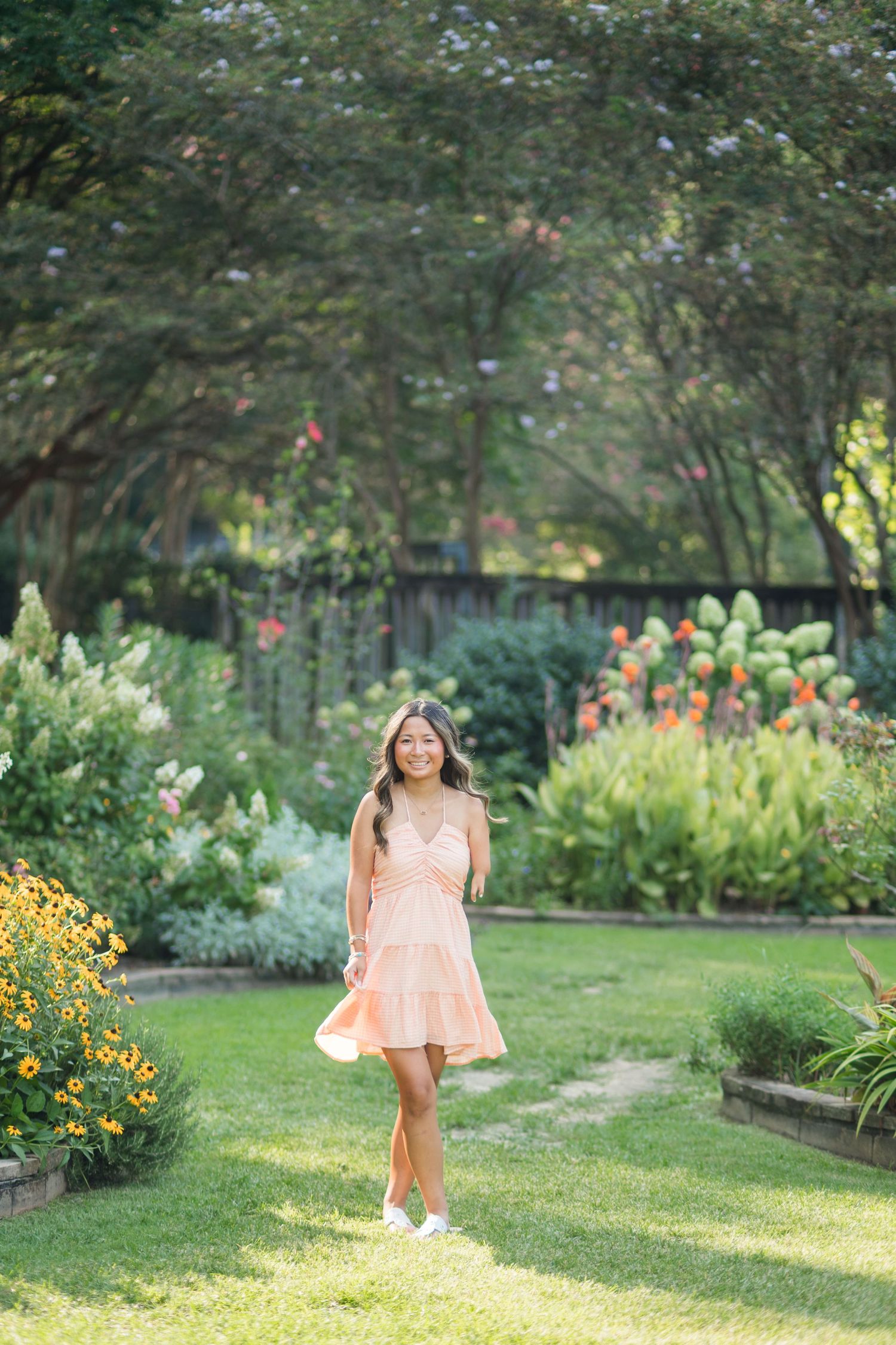 Young woman in peach dress twirling in lush garden with colorful flowers and green trees.
