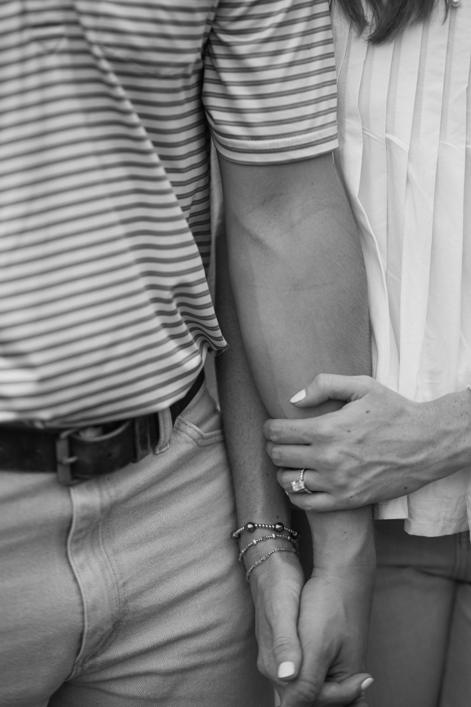 Black and white close-up of couple holding hands showing engagement ring and bracelets.