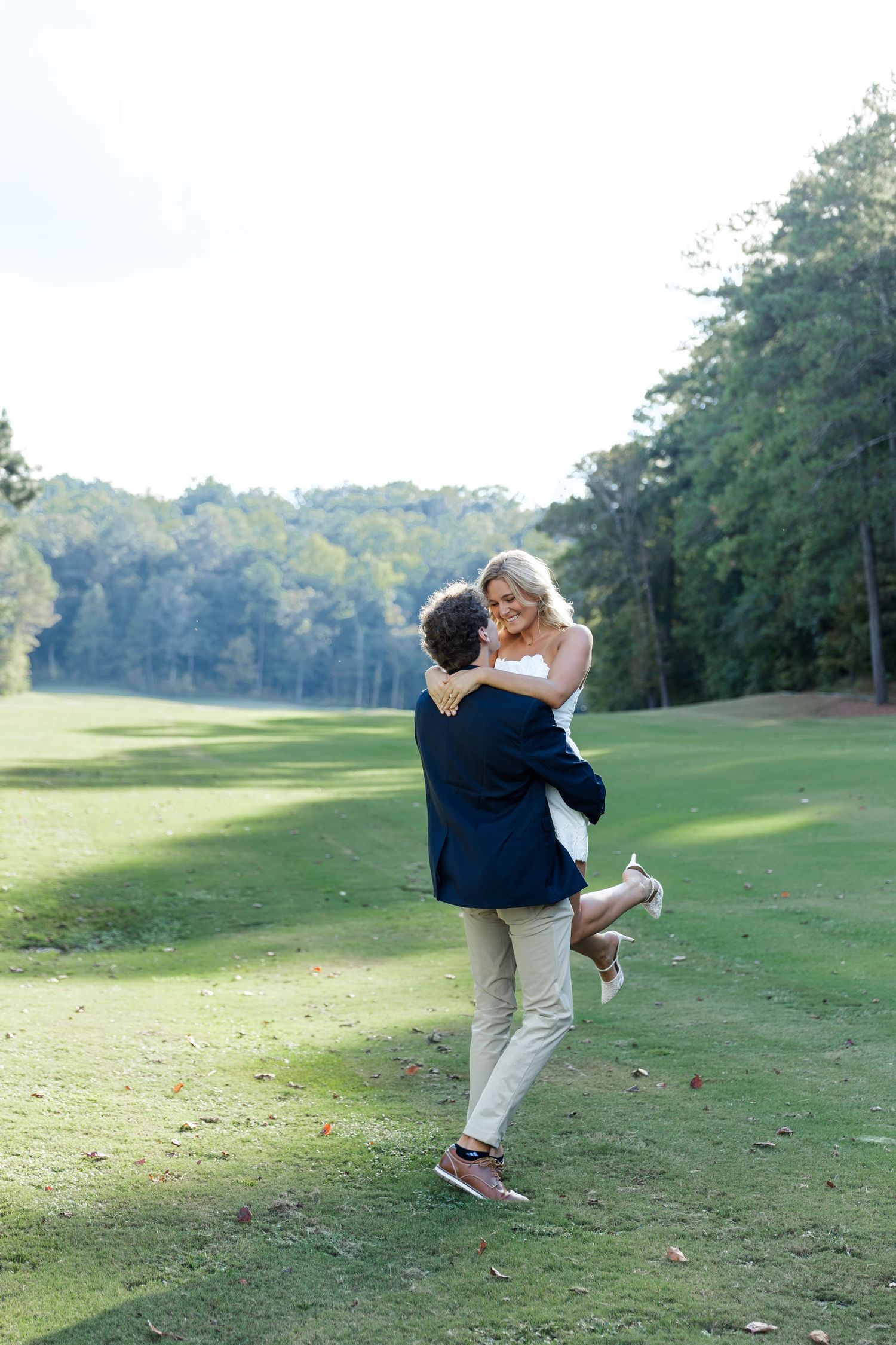 Man lifting woman in white dress on lush green golf course fairway.