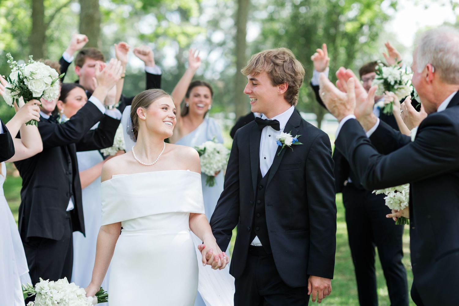 Bride and groom walking through cheering wedding party after outdoor ceremony celebration.