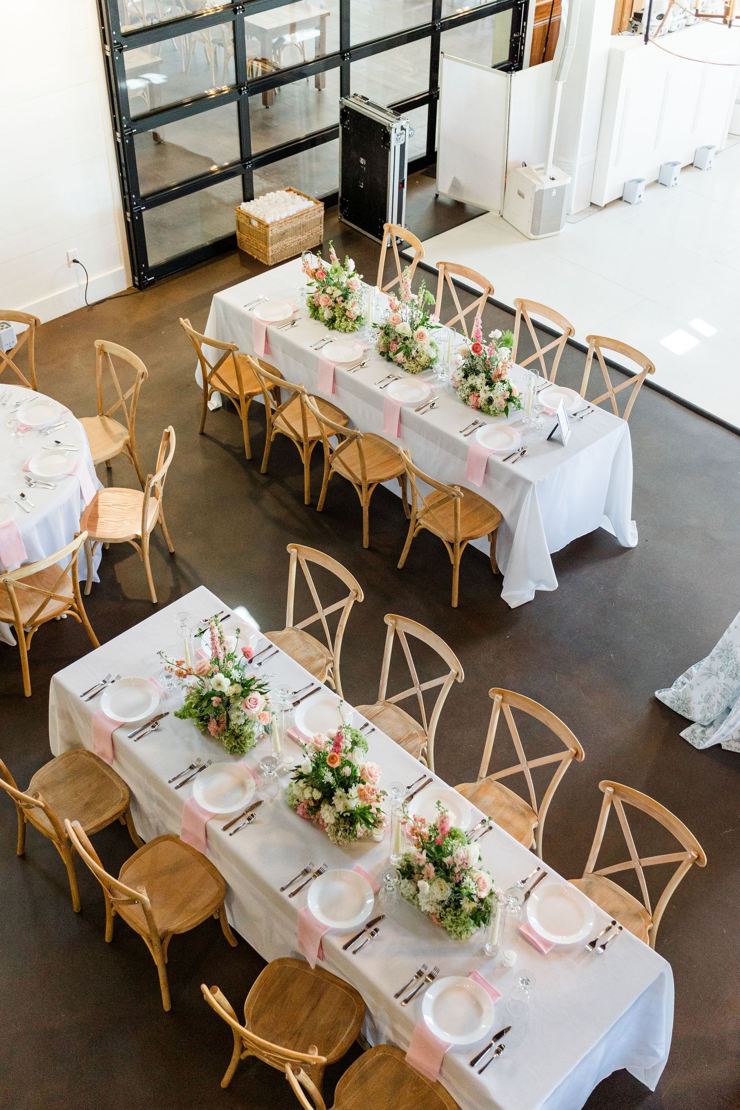 Aerial view of elegant wedding reception tables with white linens, pink ribbons, floral centerpieces, and wooden cross-back chairs.