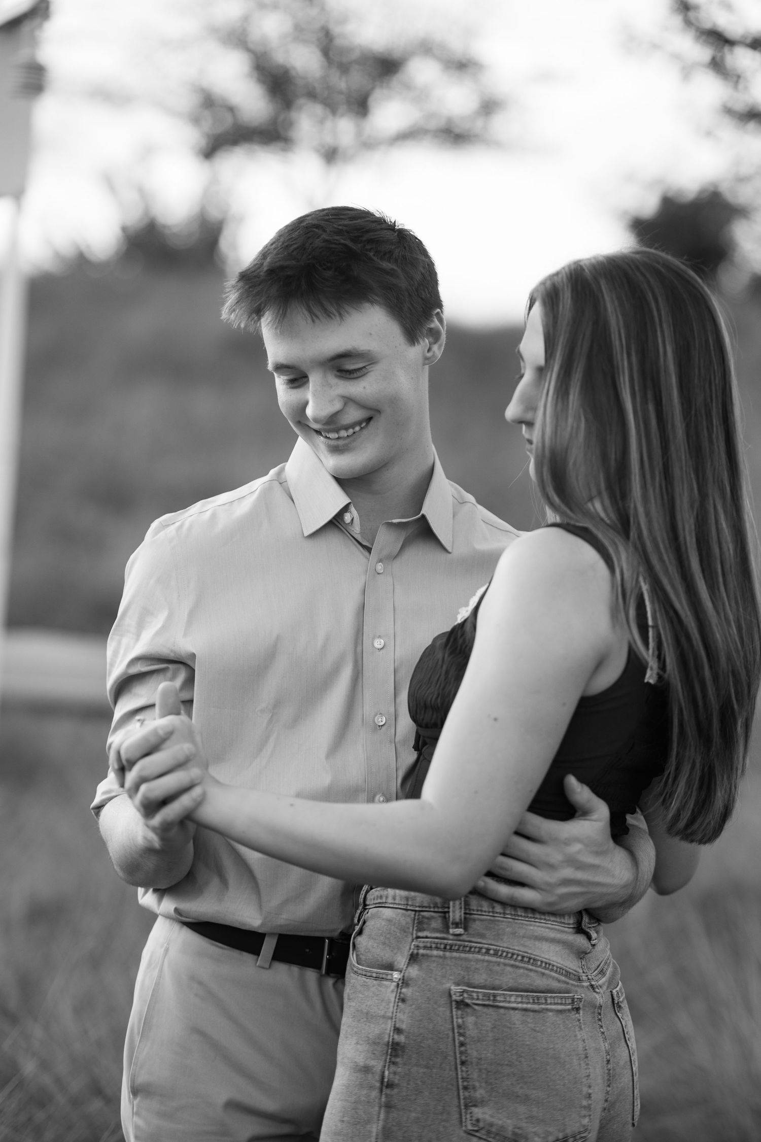 Black and white photo of young couple slow dancing outdoors, smiling and holding each other close.