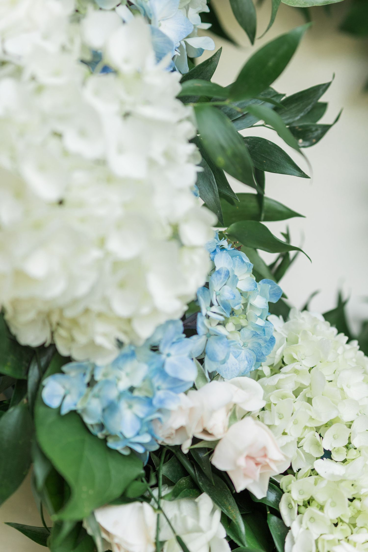 Close-up of elegant wedding arch decorated with white and blue hydrangeas, blush roses, and lush green foliage.