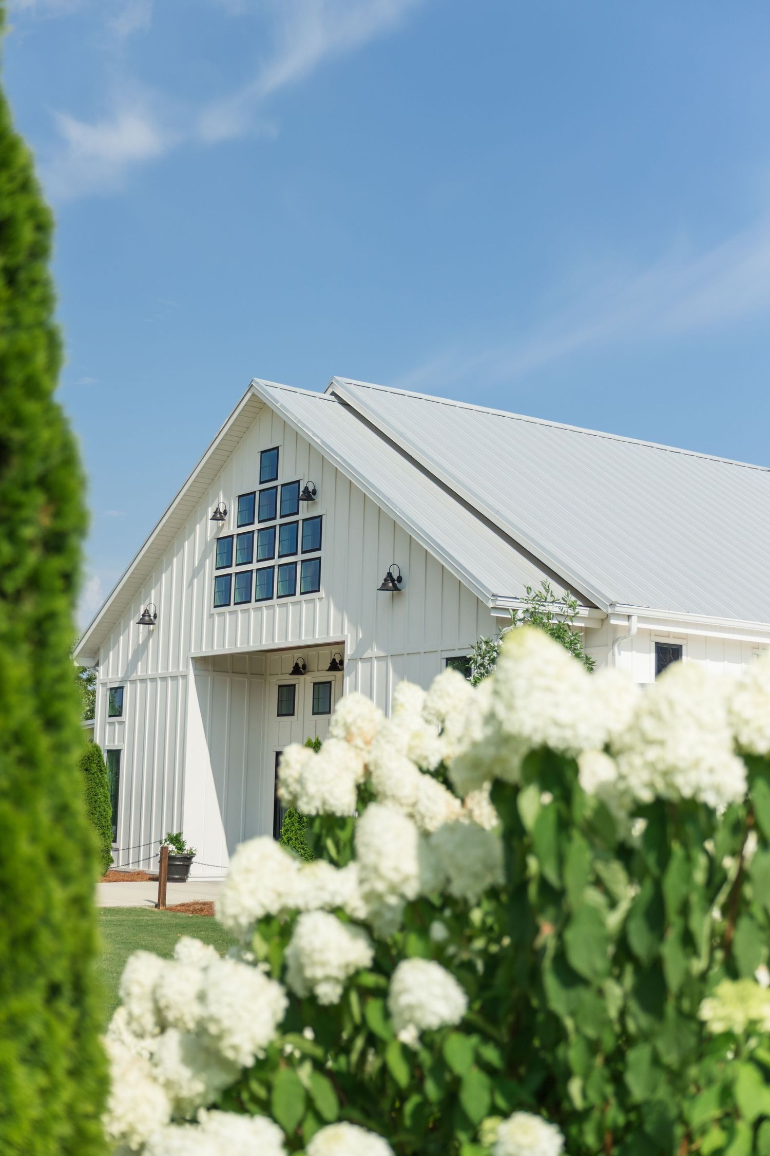White barn wedding venue with hydrangeas and blue sky in the foreground.