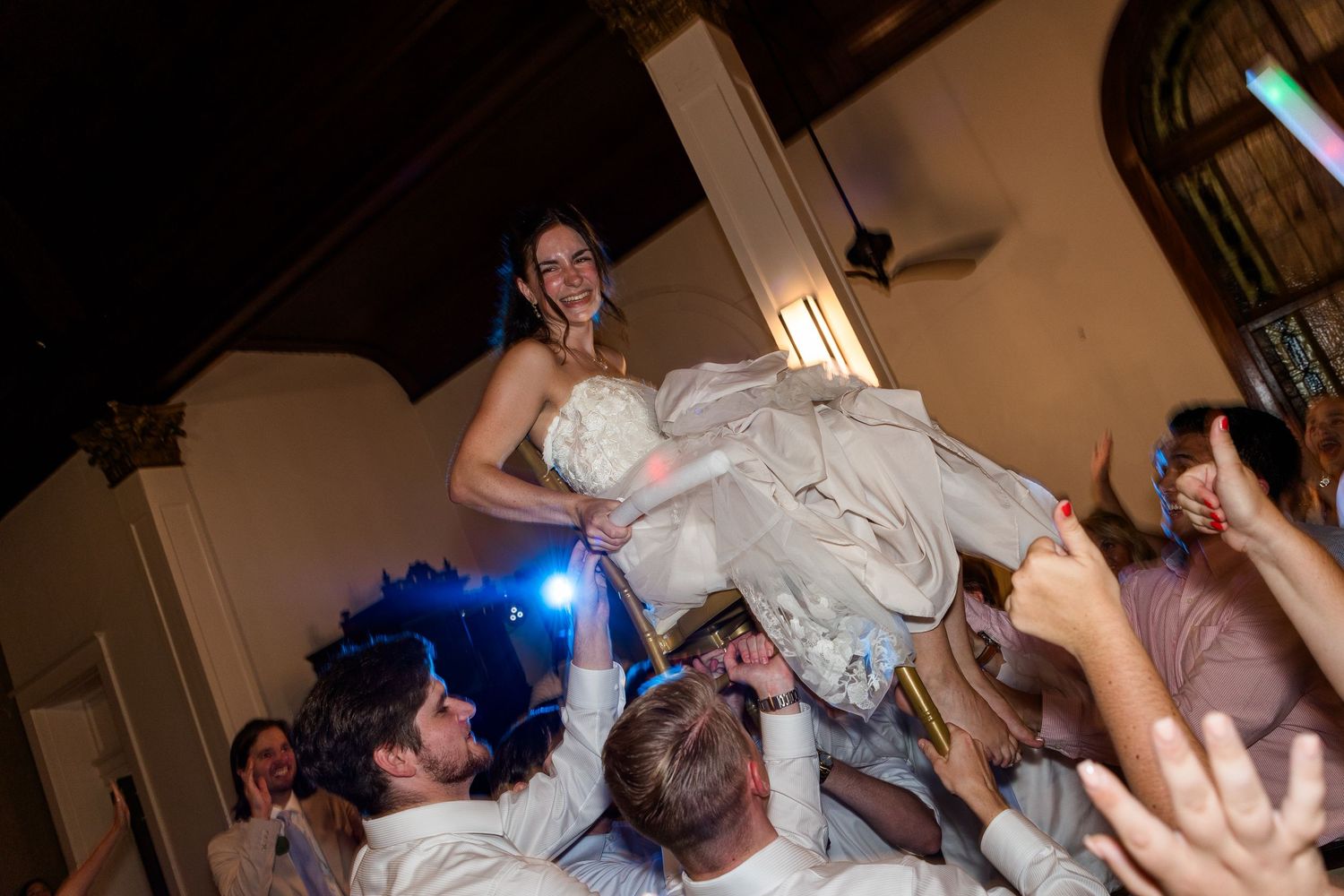 Bride being lifted by wedding guests during energetic reception dance floor celebration.